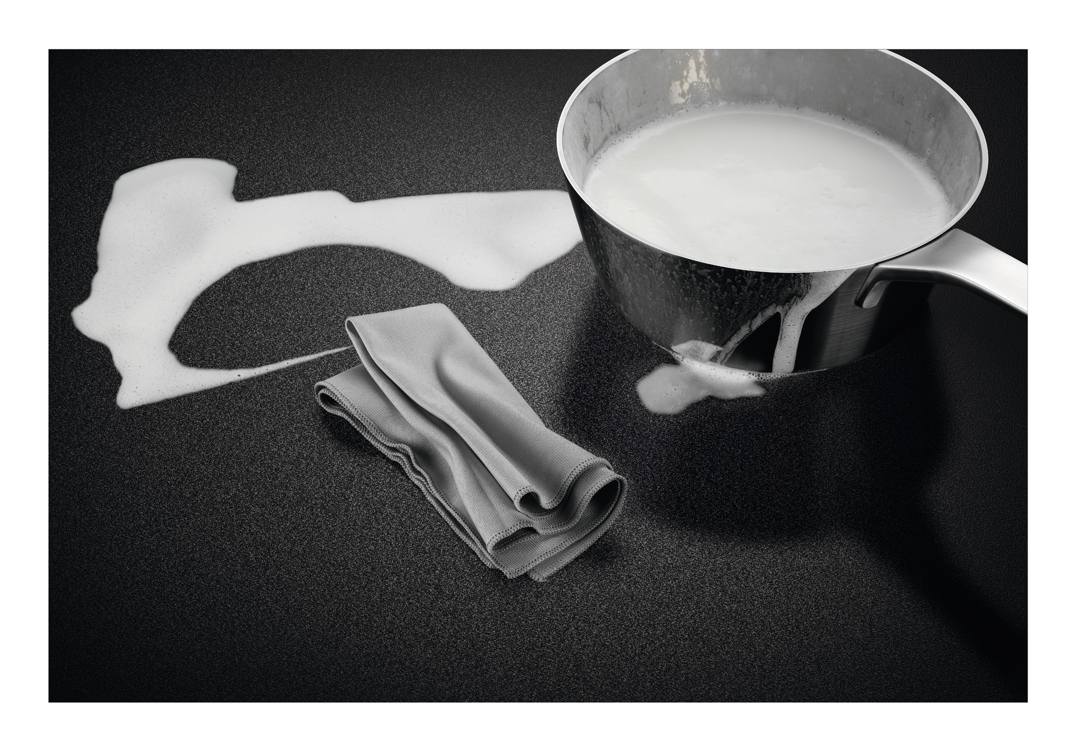 Una pentola con liquido bianco e schiuma su superficie nera accanto a un panno grigio.