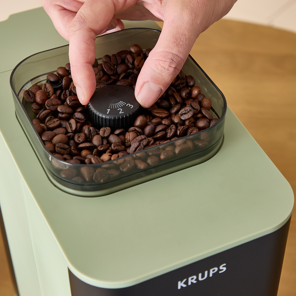 Una mano gira una manopola con numeri 1, 2, 3 in mezzo a chicchi di caffè.