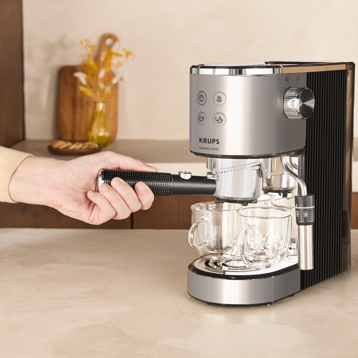 Una mano tiene il portafiltro di una macchina per espresso Krups argentata sopra due bicchieri.