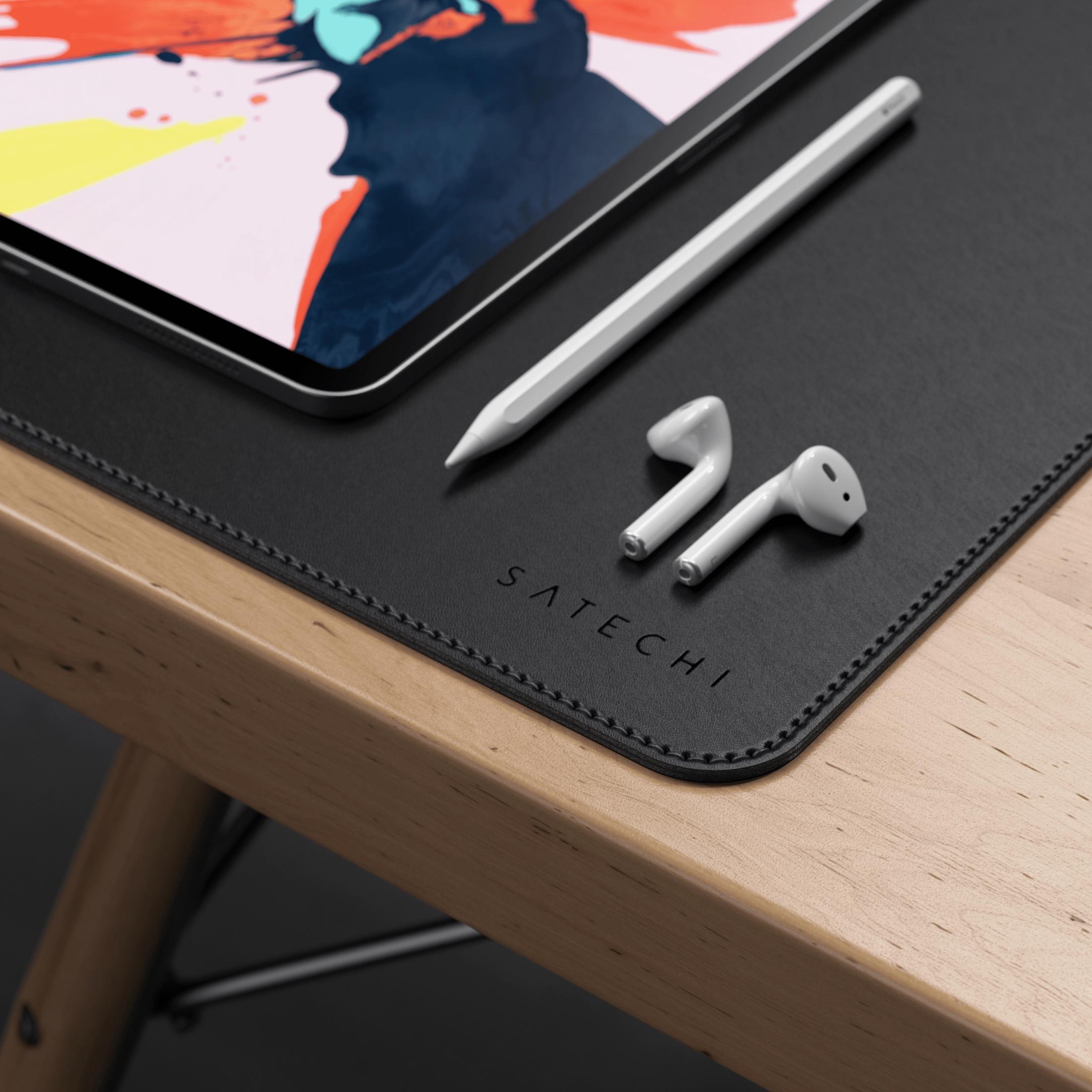 Un tablet con arte astratta, stilo e auricolari su tappetino nero su scrivania di legno.
