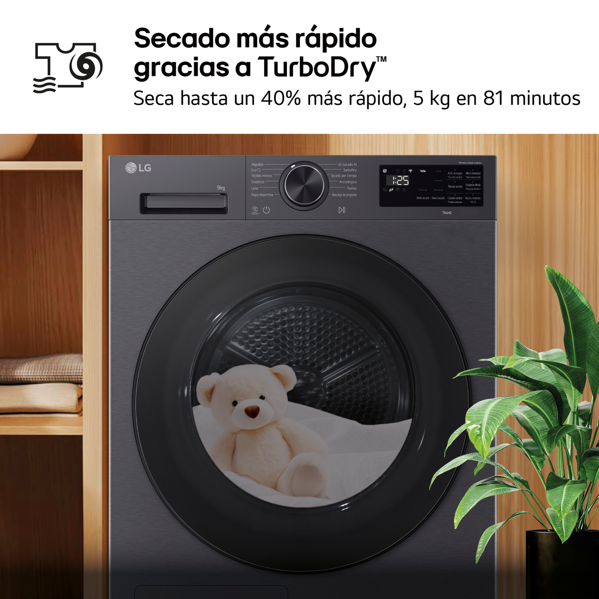 Una secadora LG gris con un osito de peluche dentro del tambor y una planta.