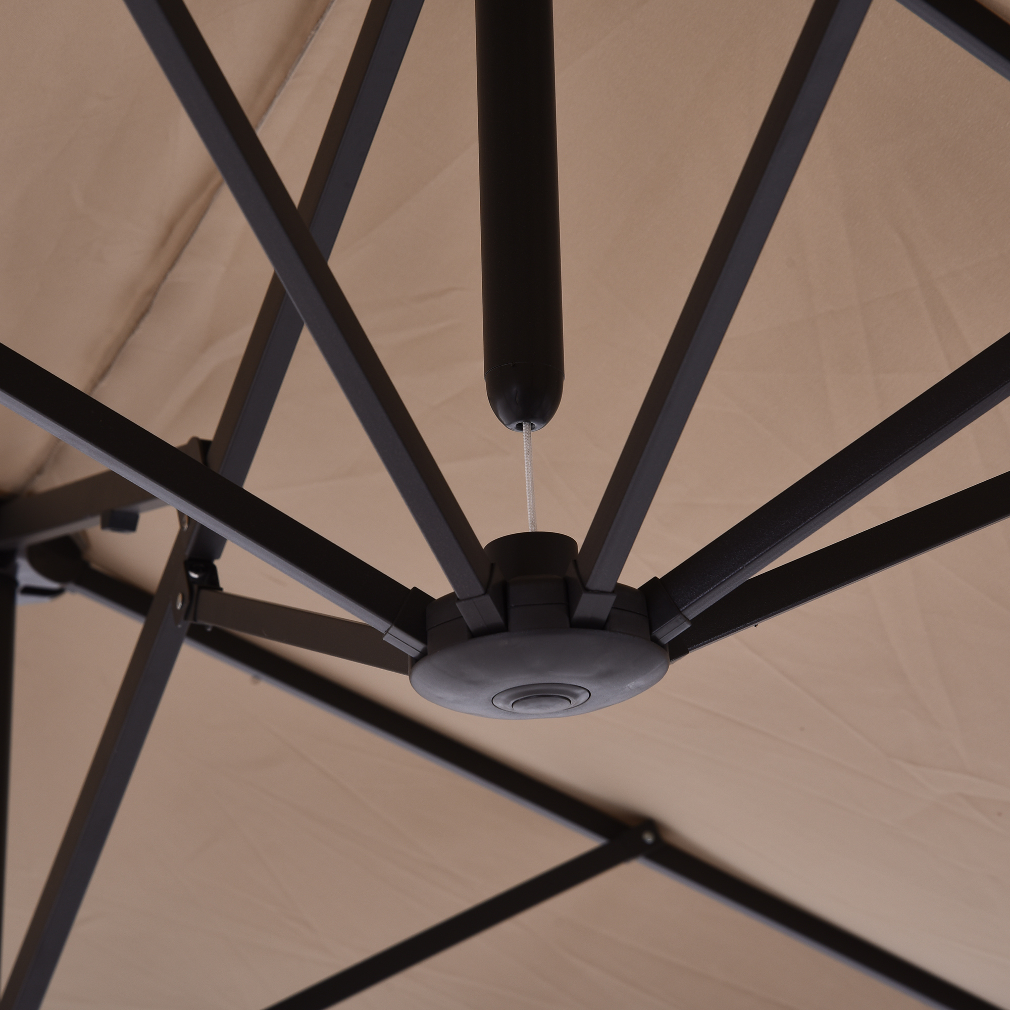 Parte inferior de un parasol con marco de metal oscuro y tela beige. Mecanismo central visible.