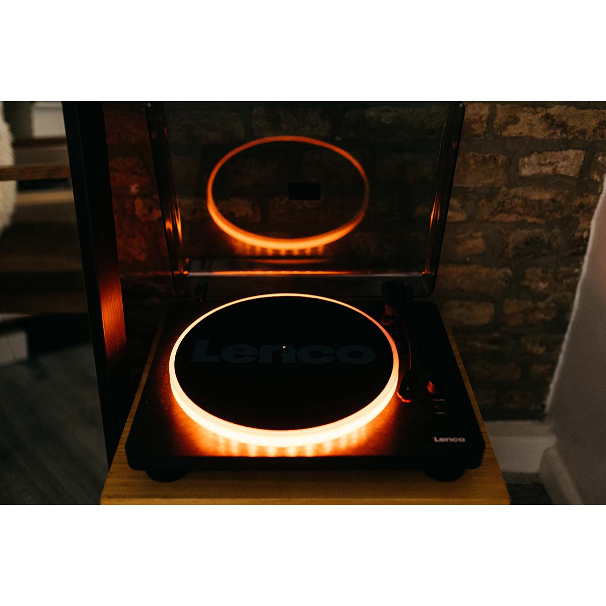 Gramofon Lenco z pomarańczowym podświetleniem na drewnianym stole.