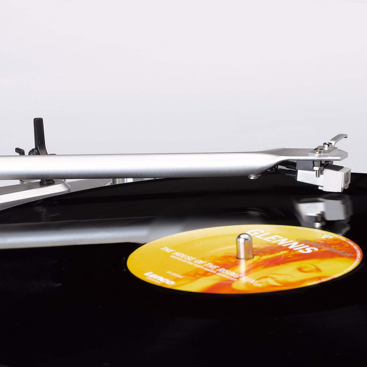 Srebrne ramię gramofonu spoczywa na czarnej płycie winylowej z żółtą etykietą.