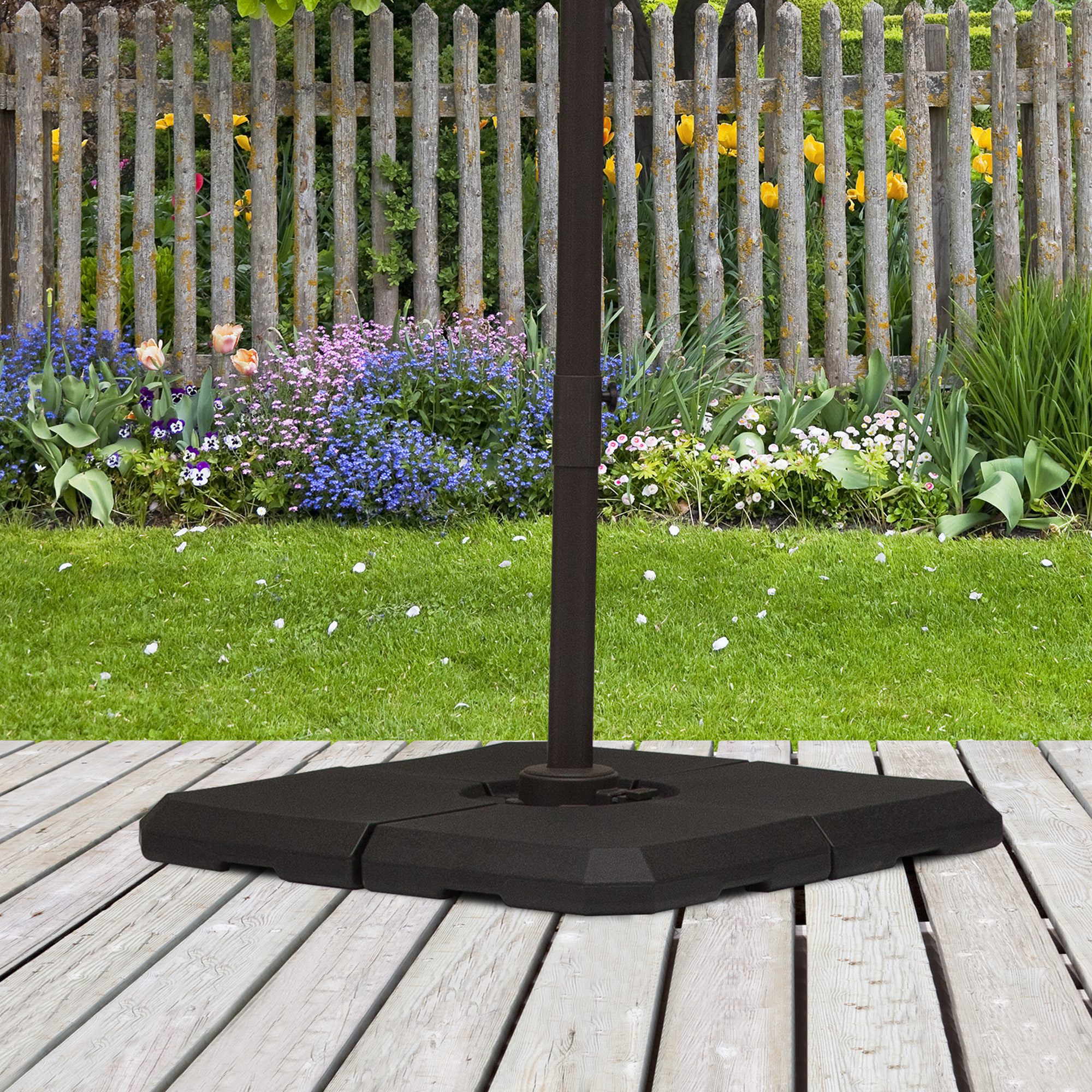 Un soporte oscuro para sombrilla en una terraza de madera frente a un jardín y valla en flor.