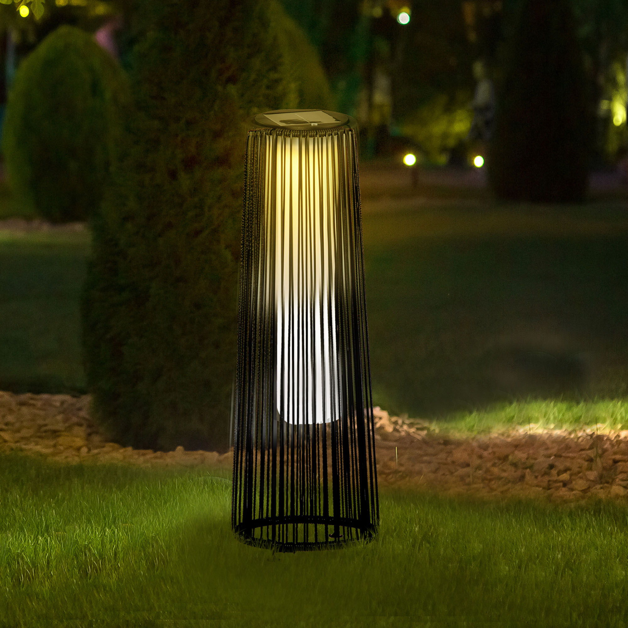 Una lámpara con barras verticales ilumina un jardín de noche.