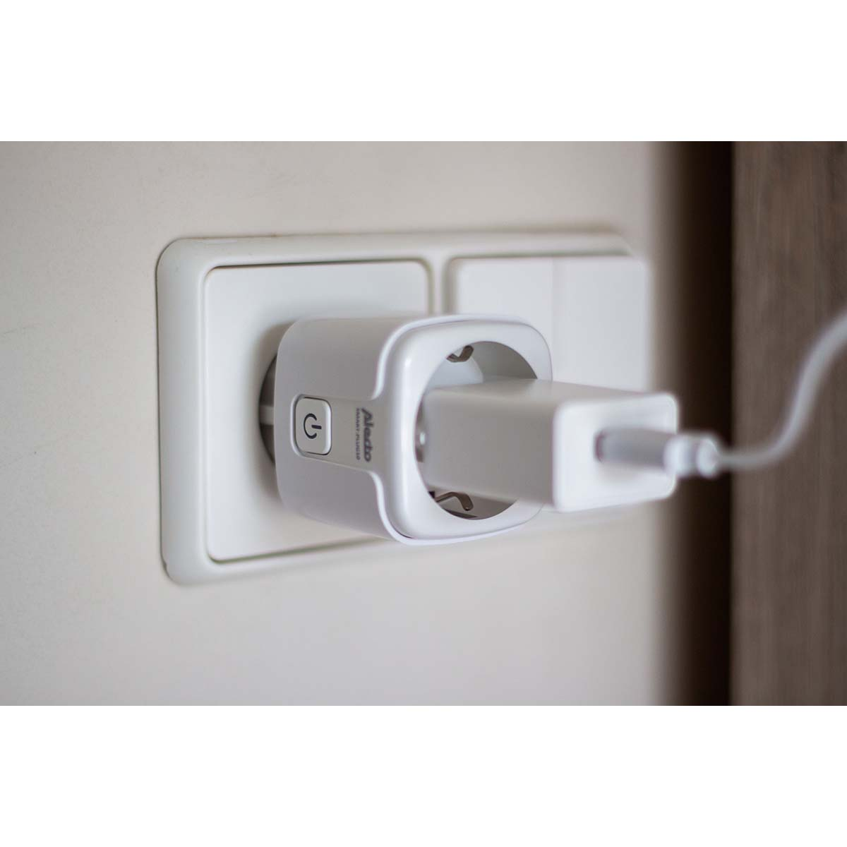 A white smart plug with a charging adapter and cable in an electrical outlet.