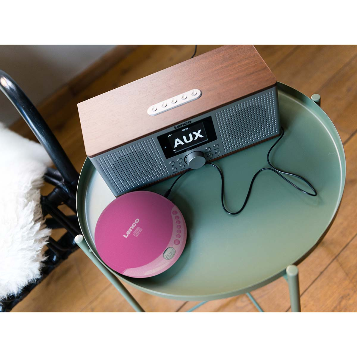 Ein Holzradio und ein rosafarbener CD-Player stehen auf einem runden, grünen Tisch.