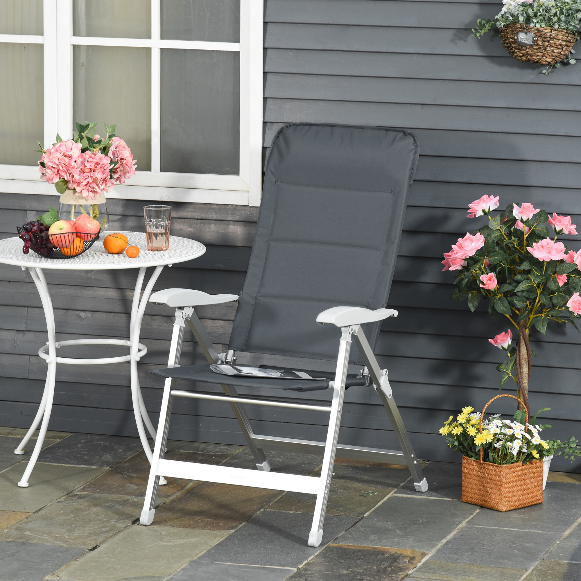 Una silla plegable oscura y mesa blanca con frutas y bebidas en un patio de piedra.