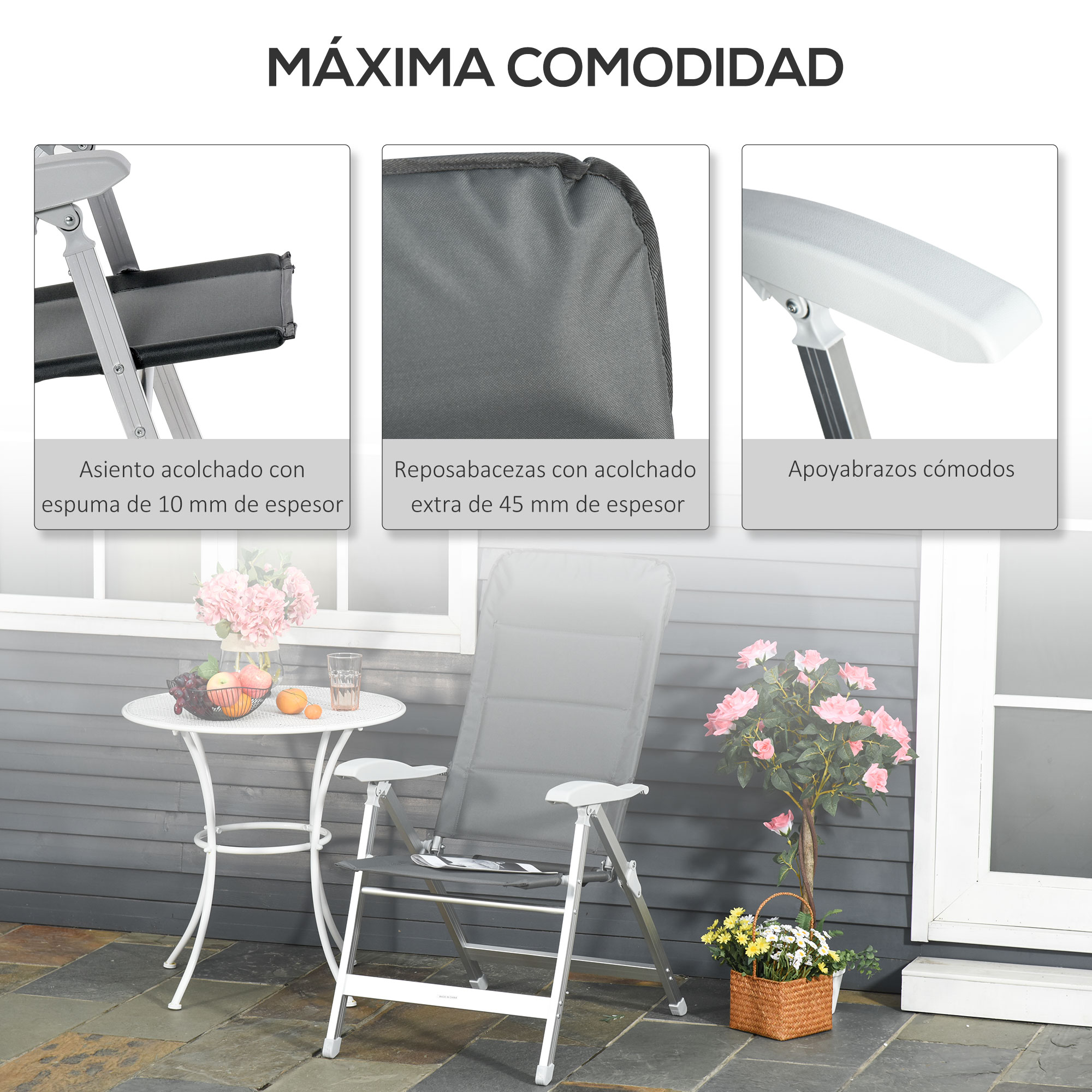 Una tumbona gris con mesa blanca y flores delante de una casa.