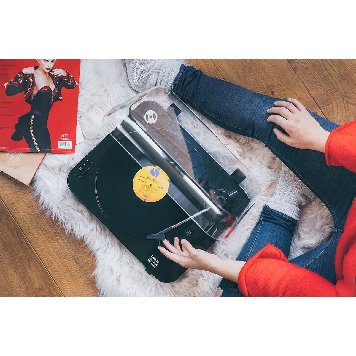 Osoba siedzi na puszystym dywanie, obsługując czarny gramofon z płytą winylową.