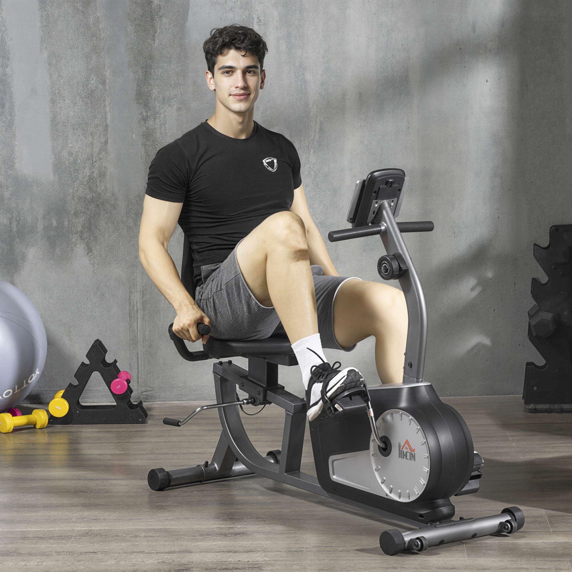 Un hombre de negro en una bicicleta estática reclinada en un gimnasio con pesas.