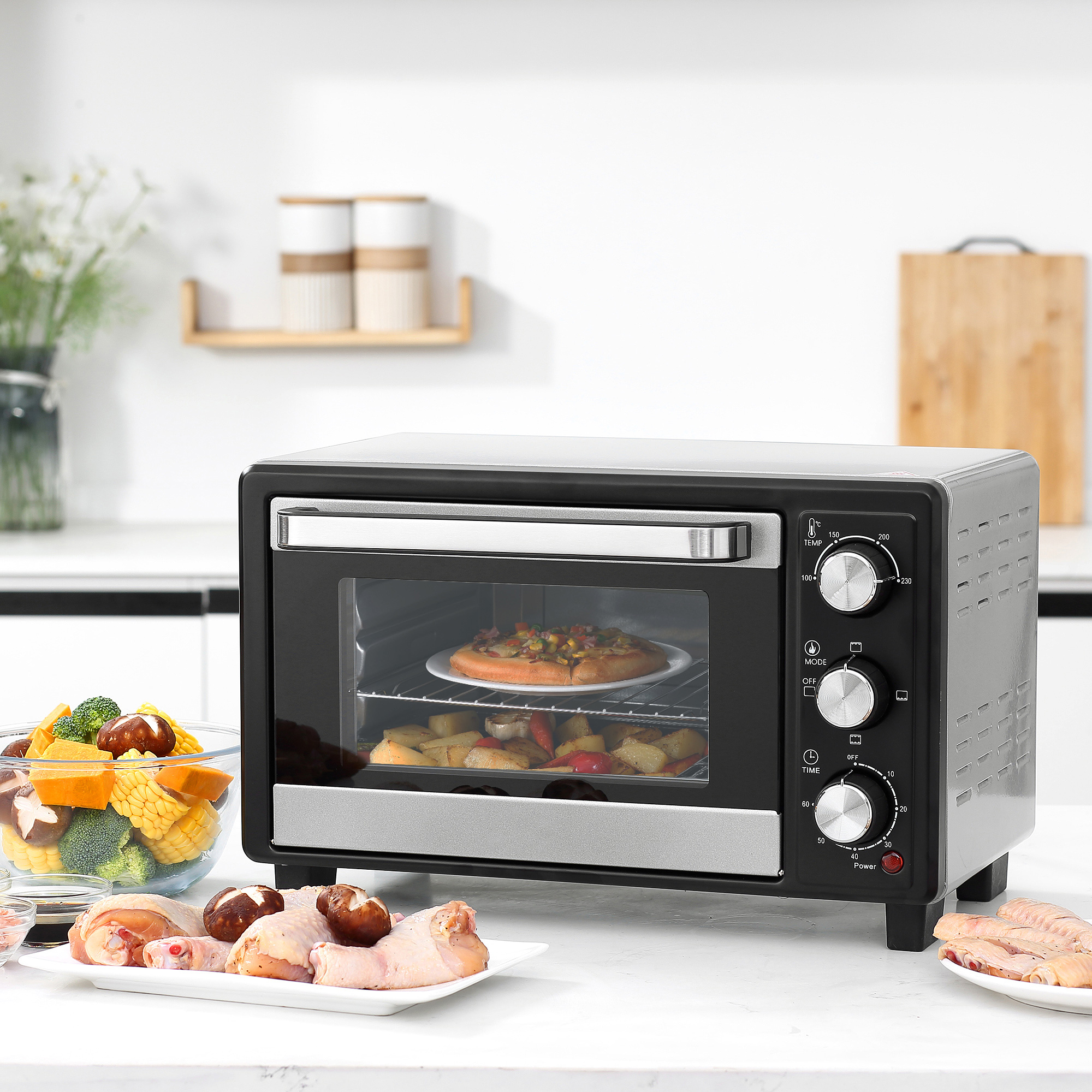 Un horno con pizza y acompañamientos. Pollo crudo y verduras están en el mostrador.