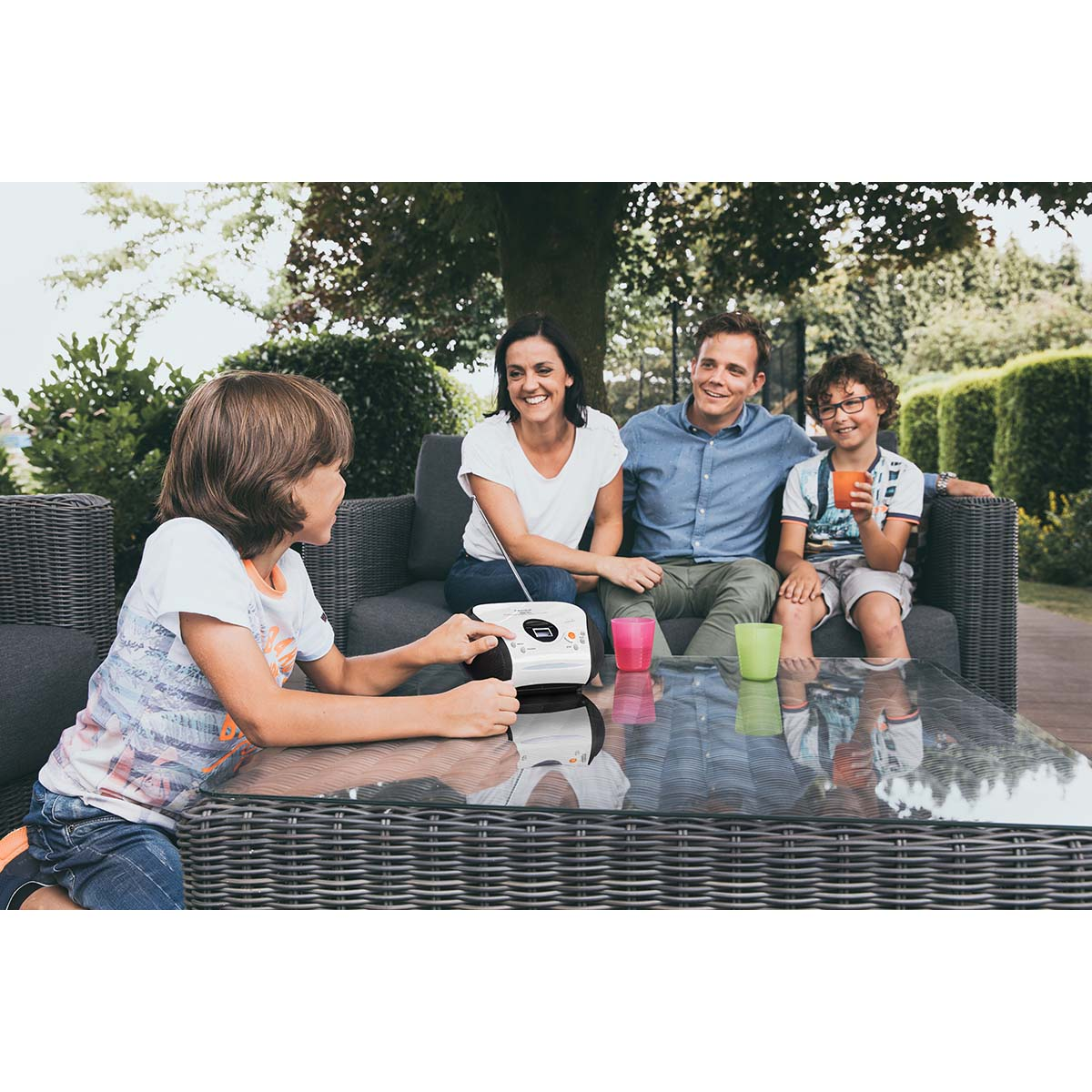 Eine Familie sitzt auf einer Couch im Garten. Ein Junge bedient ein Radio.