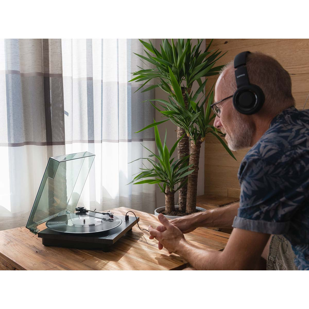 Mężczyzna w słuchawkach słucha muzyki z gramofonu, obok roślin.