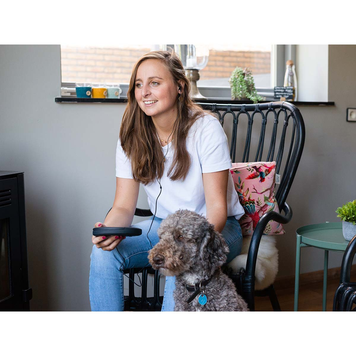 Kobieta siedzi na krześle z psem, trzymając pilota.