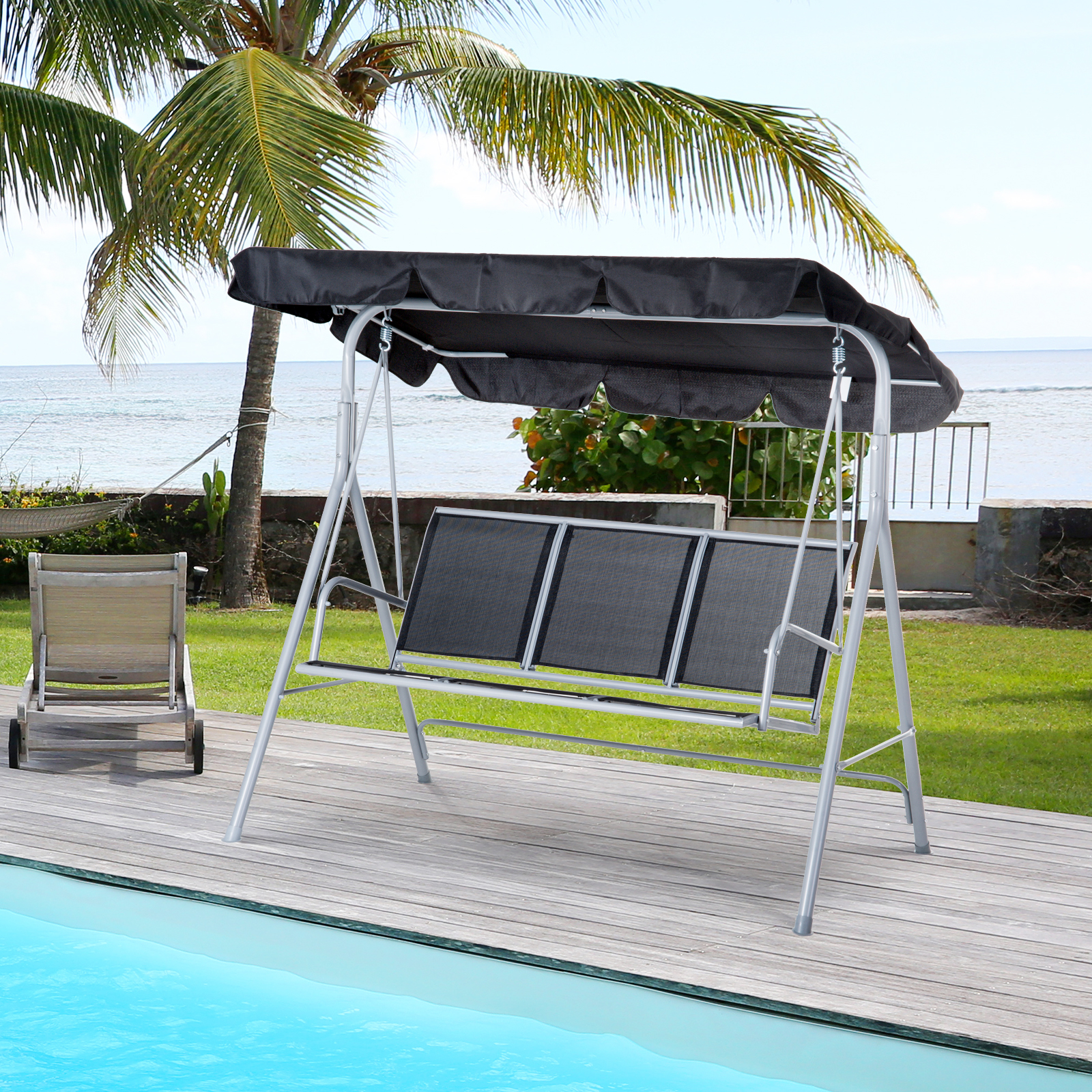 Una seduta a dondolo con tettoia nera si trova su un ponte di legno vicino a una piscina, con palme e l'oceano sullo sfondo.