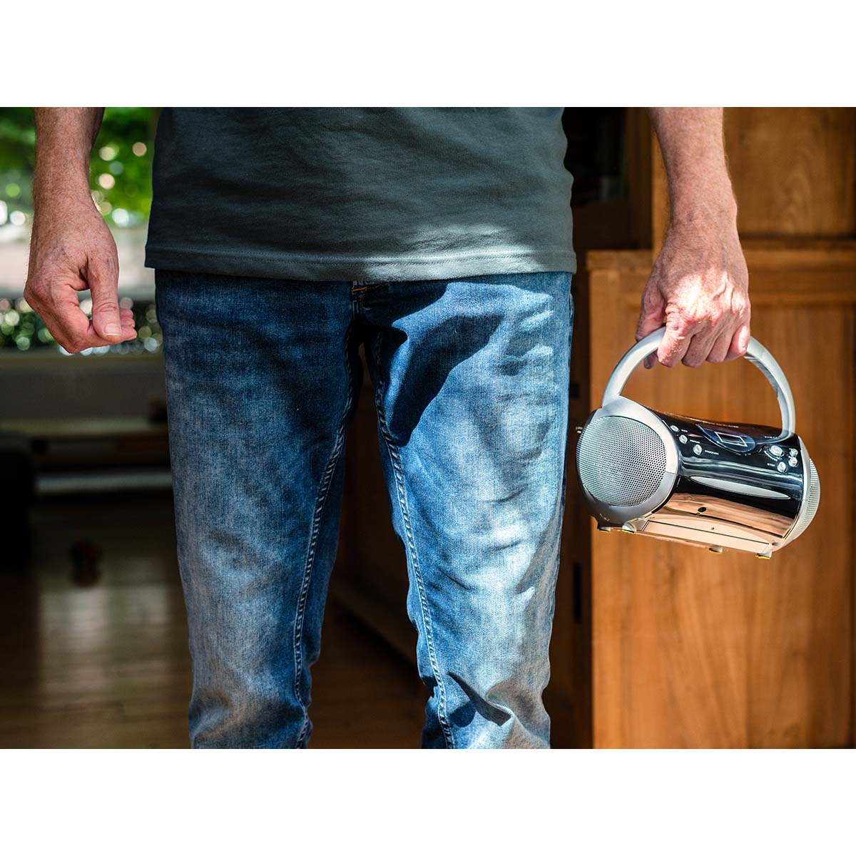 Man in jeans holding a silver boombox radio with a handle.