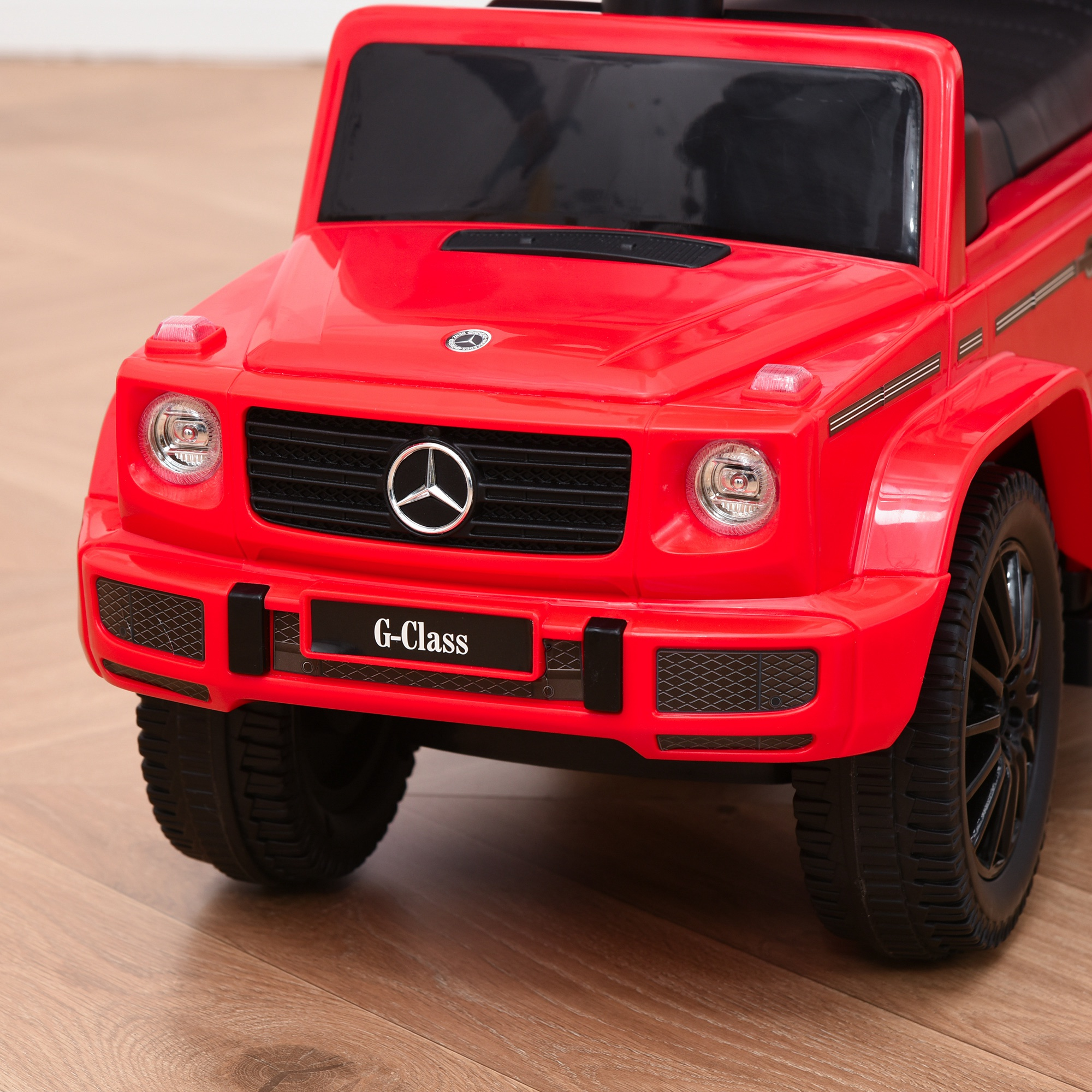 Un coche de juguete rojo, estilo Mercedes G-Class, sobre suelo de madera.