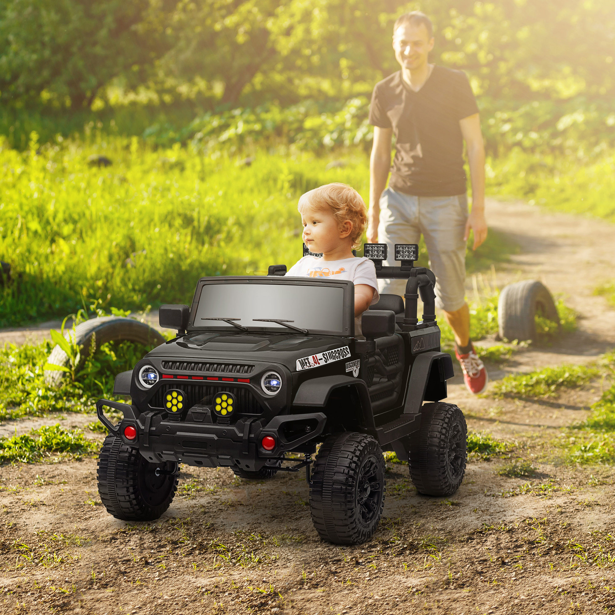 Un niño se sienta en un jeep de juguete negro mientras un hombre camina detrás por un camino de tierra.