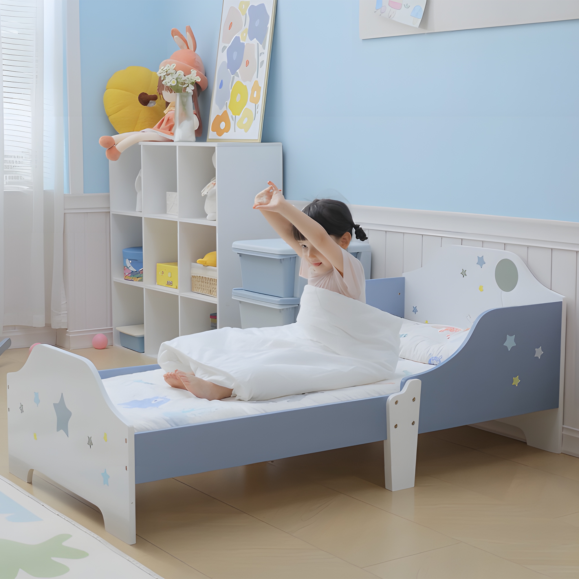 Una niña pequeña se sienta en una cama azul con estrellas, estirando los brazos.