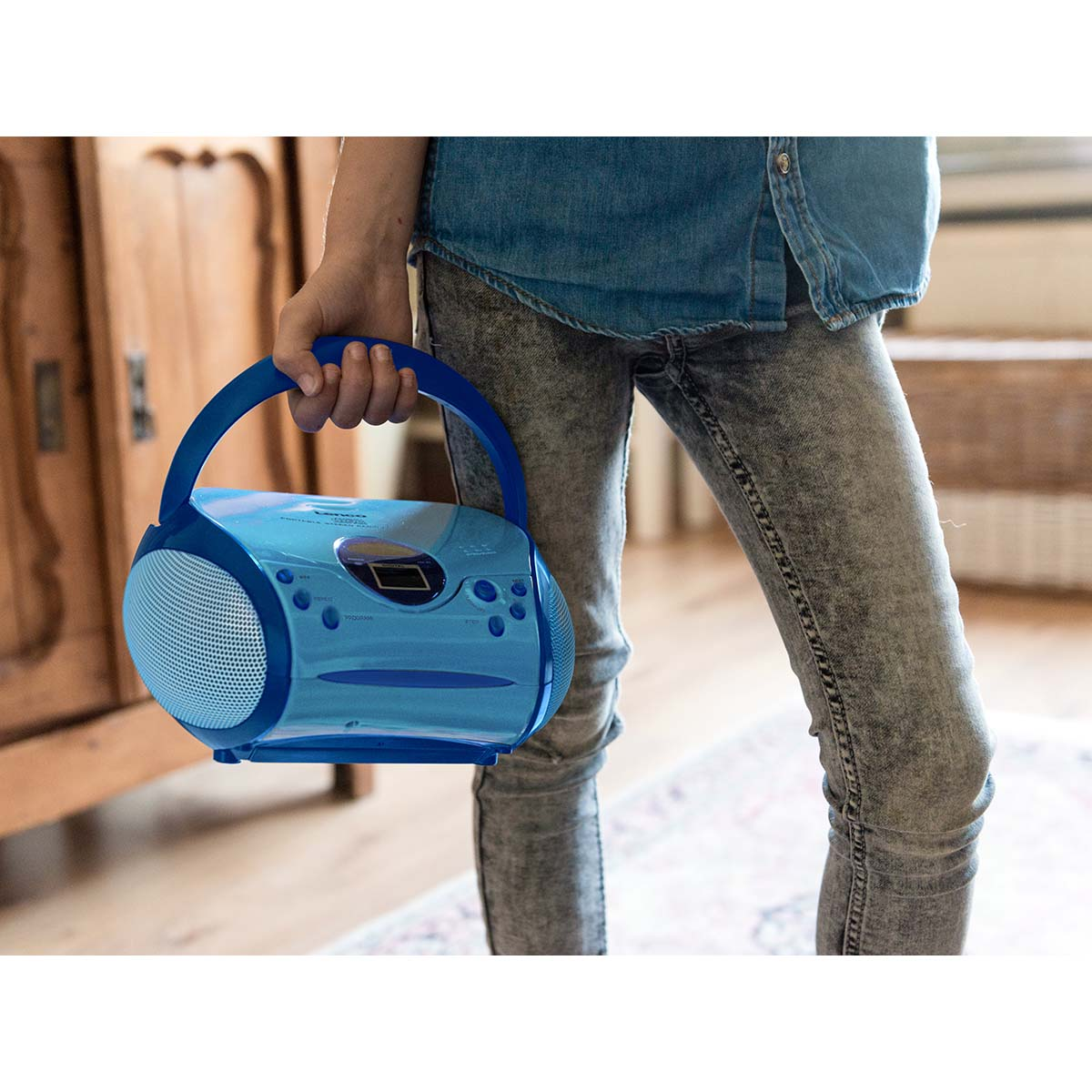 Eine Person in Jeans hält einen blauen Boombox-CD-Player mit Tragegriff.