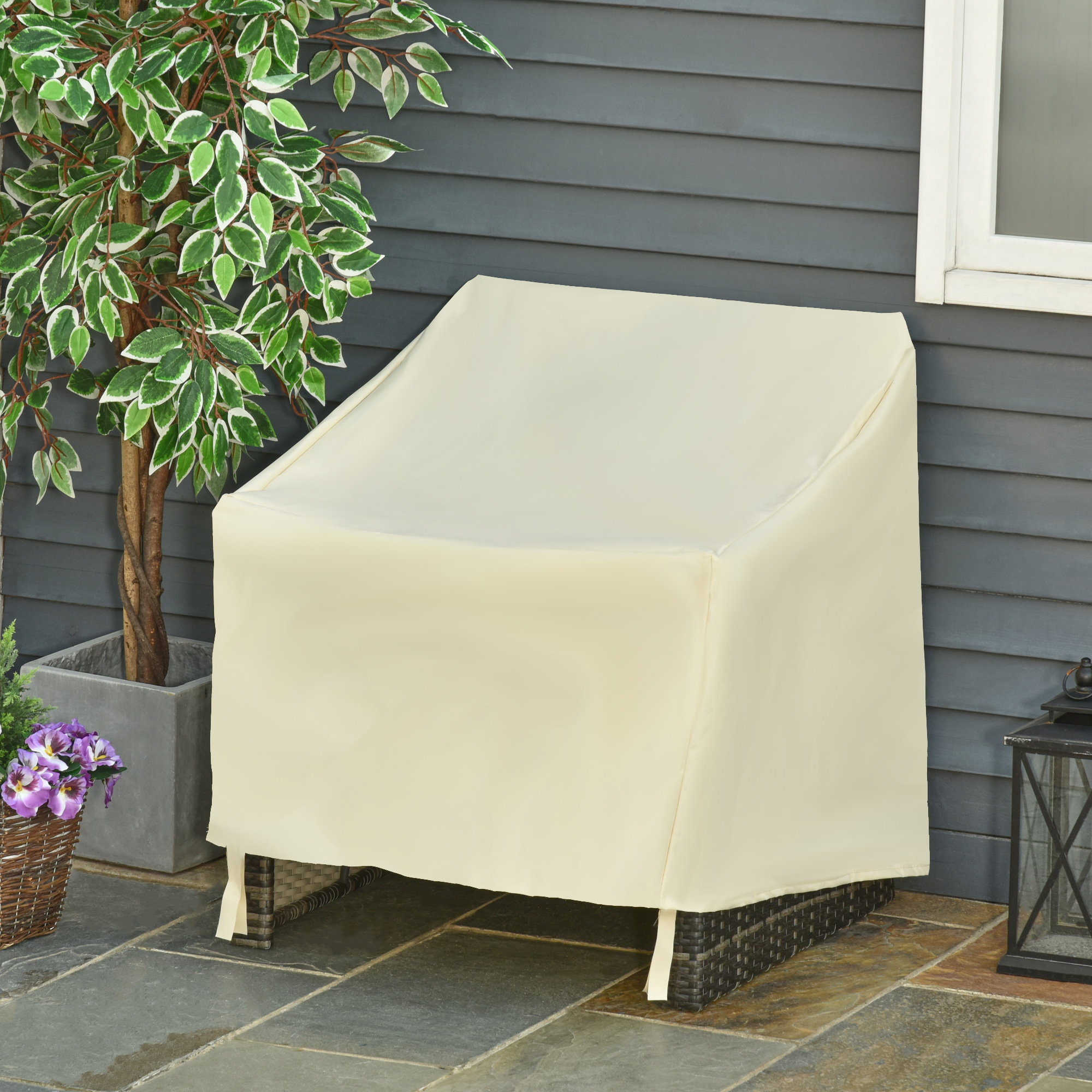 Una funda color crema cubre un sillón de exterior junto a una planta y un farol.