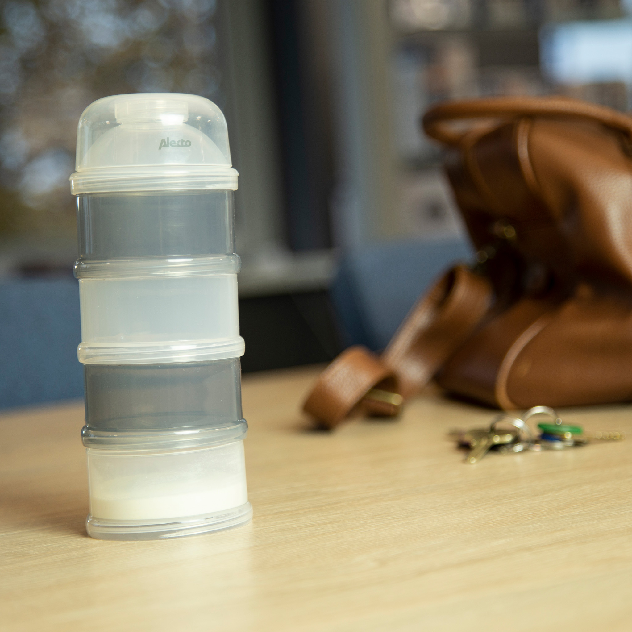 A stacked formula dispenser with a brown leather bag and keys on a wooden table.