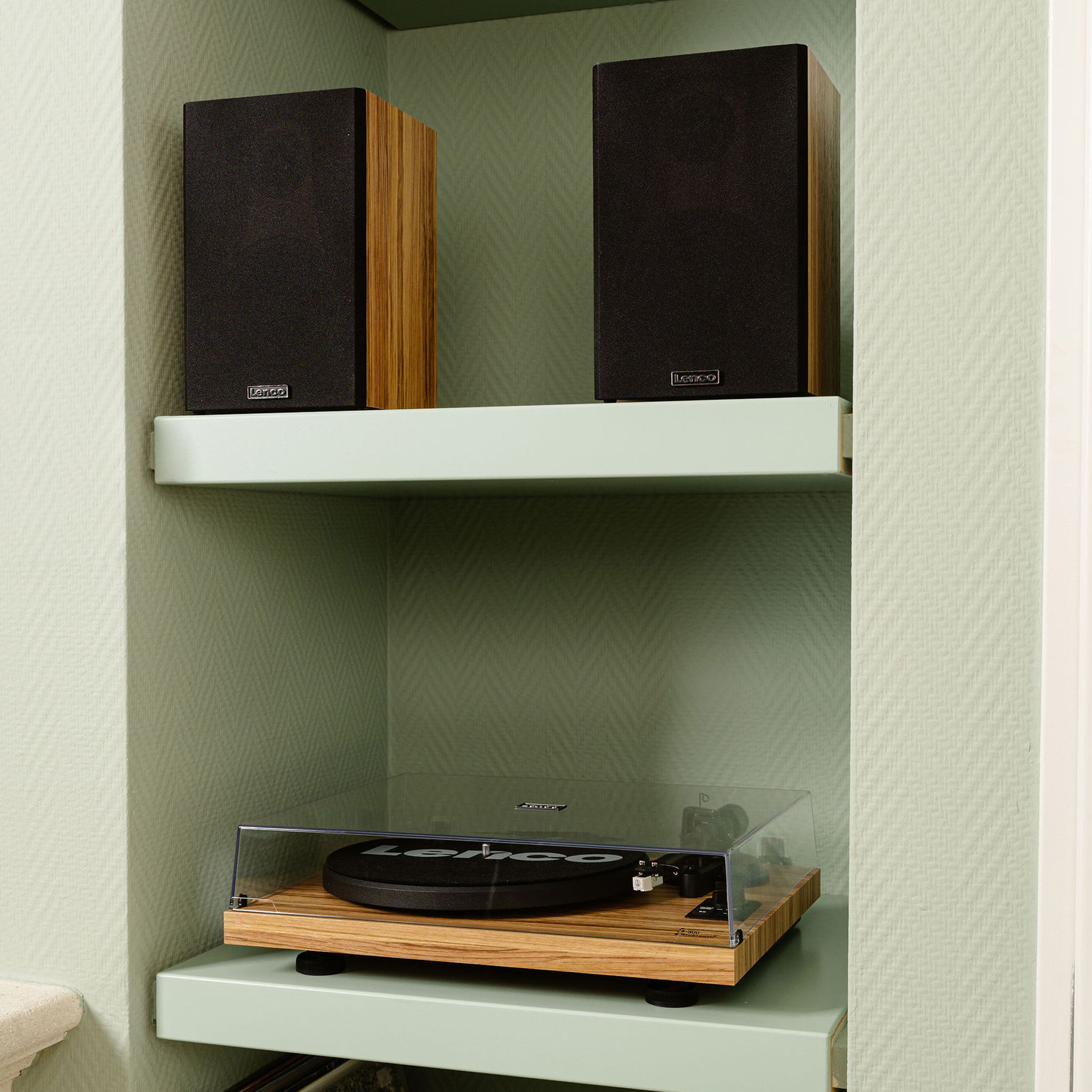 Dwa czarne głośniki i gramofon na jasnozielonych półkach.