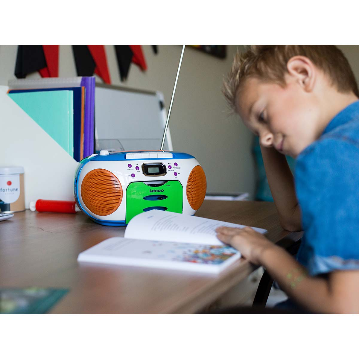 Un niño lee un libro junto a un boombox colorido con reproductor de CD.