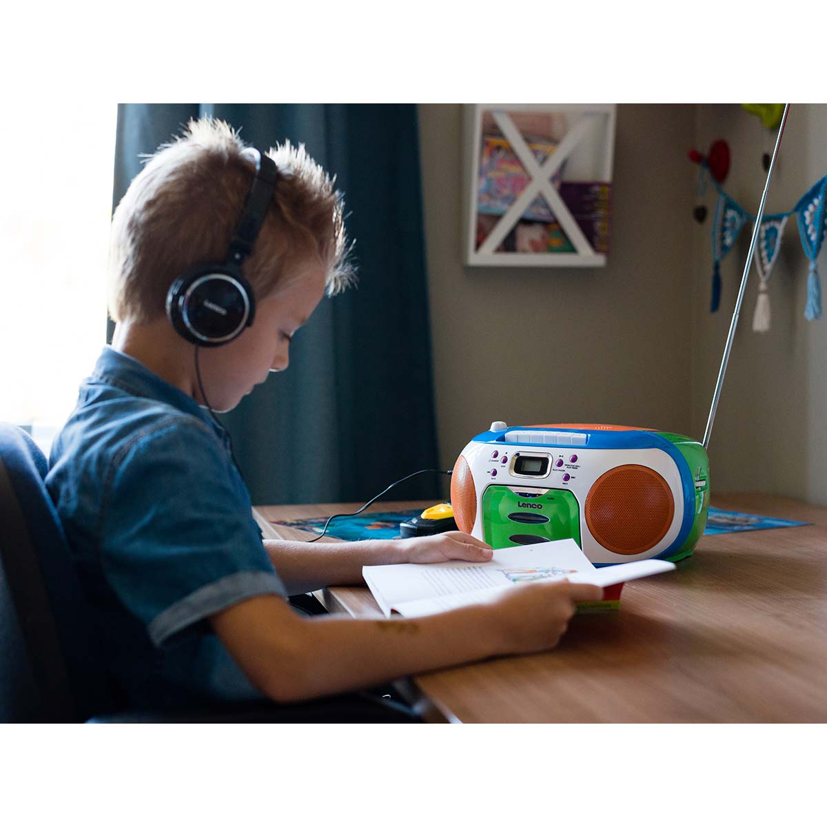 Un niño con auriculares lee un libro junto a un radiocasete de colores.