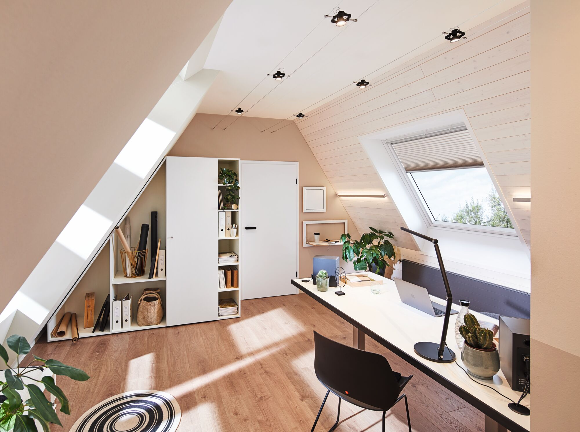 Ein Arbeitsplatz unter einer Dachschräge mit Schreibtisch, Lampe und Laptop.