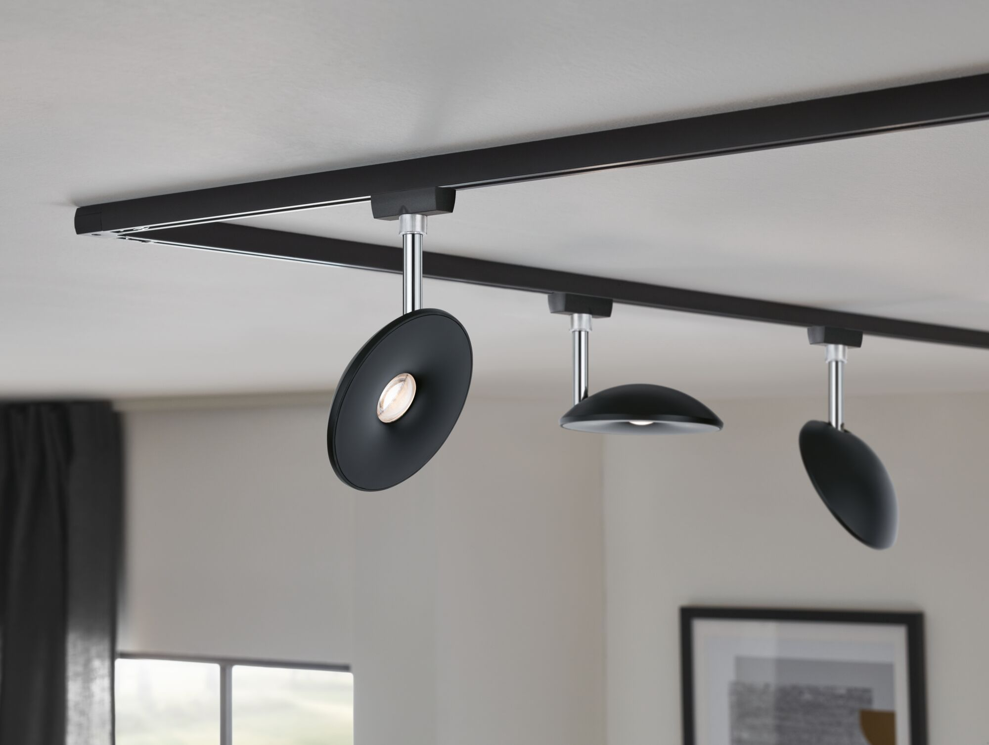 Schwarze Schienenbeleuchtung mit drei verstellbaren Strahlern an weißer Decke.