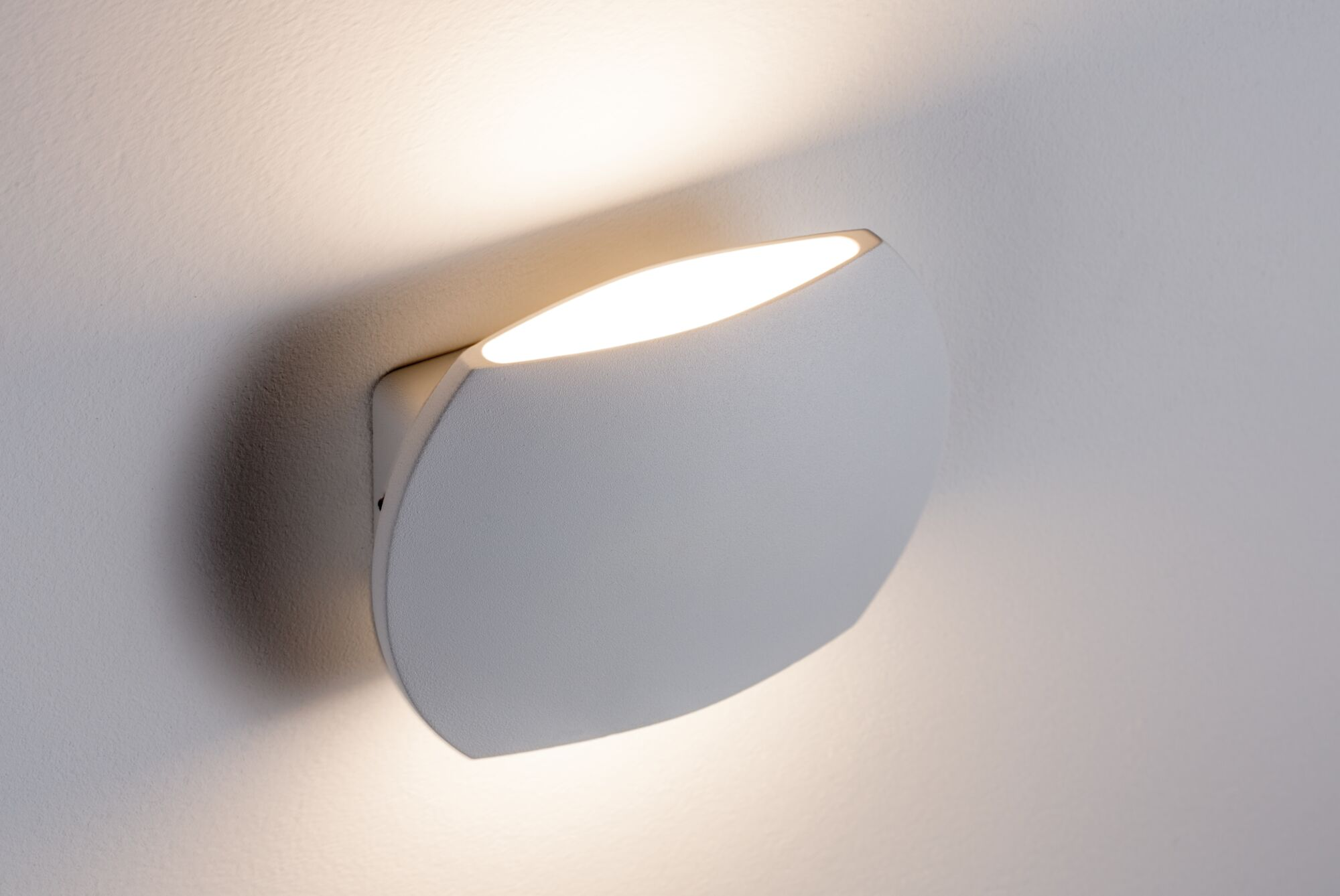 Ein moderner, weißer Wandleuchter mit einem leuchtenden Spalt oben, der die Wand beleuchtet.