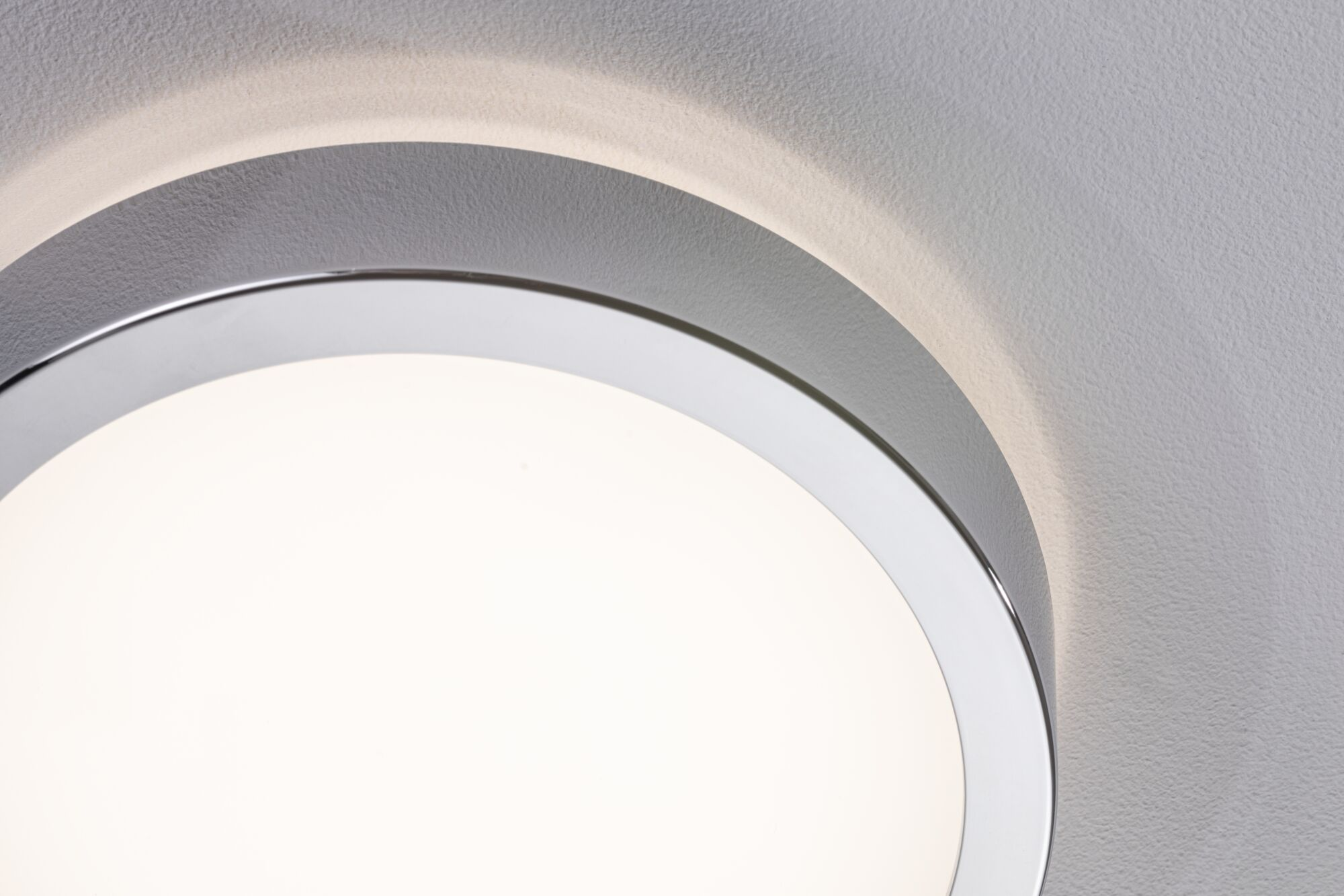 Ein Teil einer runden, hellen Lampe mit silbernem Rand auf einer strukturierten Wand.