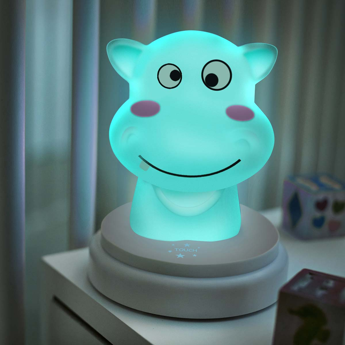 Eine leuchtende Hippo-Lampe in Türkis steht auf einem Nachttisch, beleuchtet von innen.