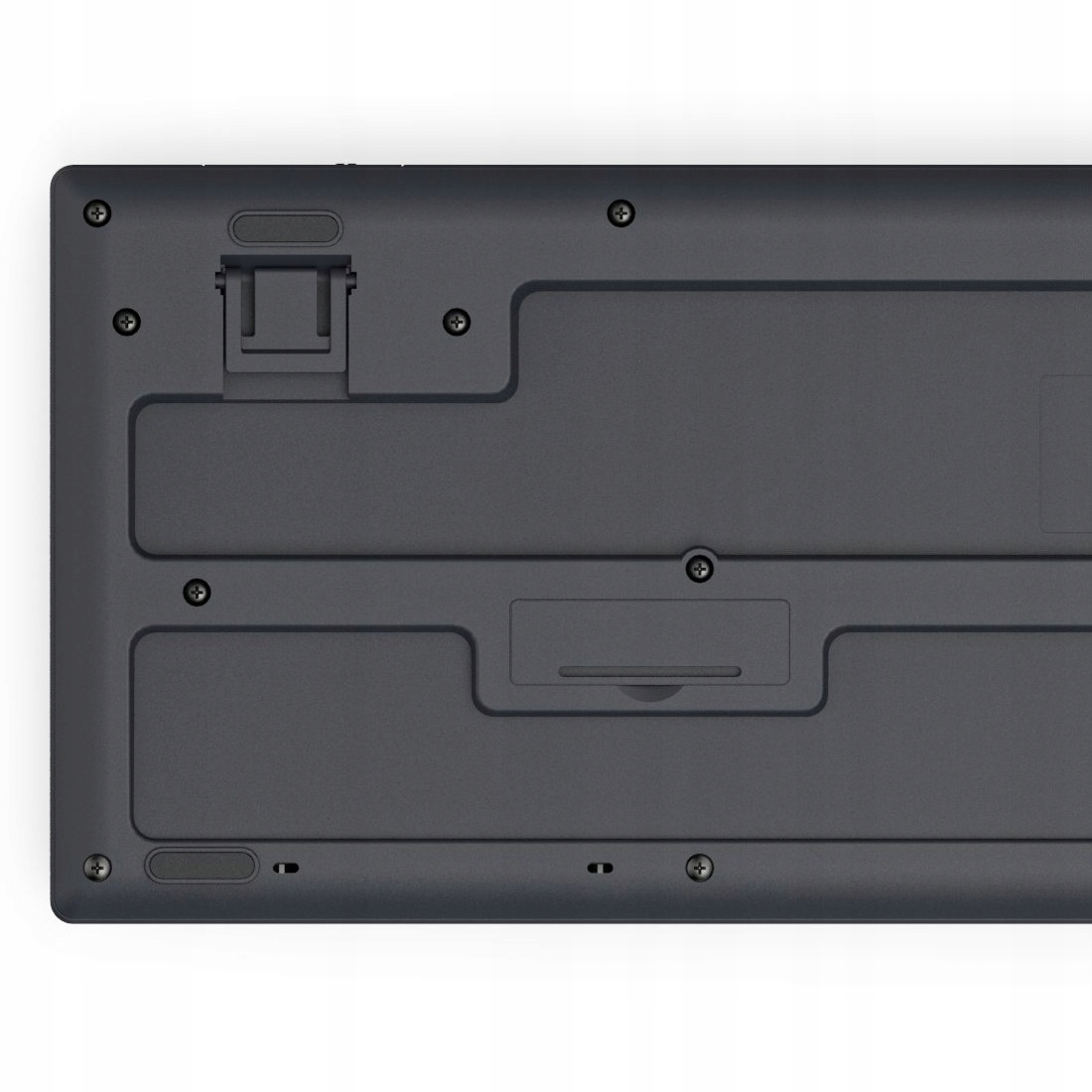 Parte inferior de un teclado gris oscuro que muestra tornillos, un soporte y la tapa del compartimento de batería.