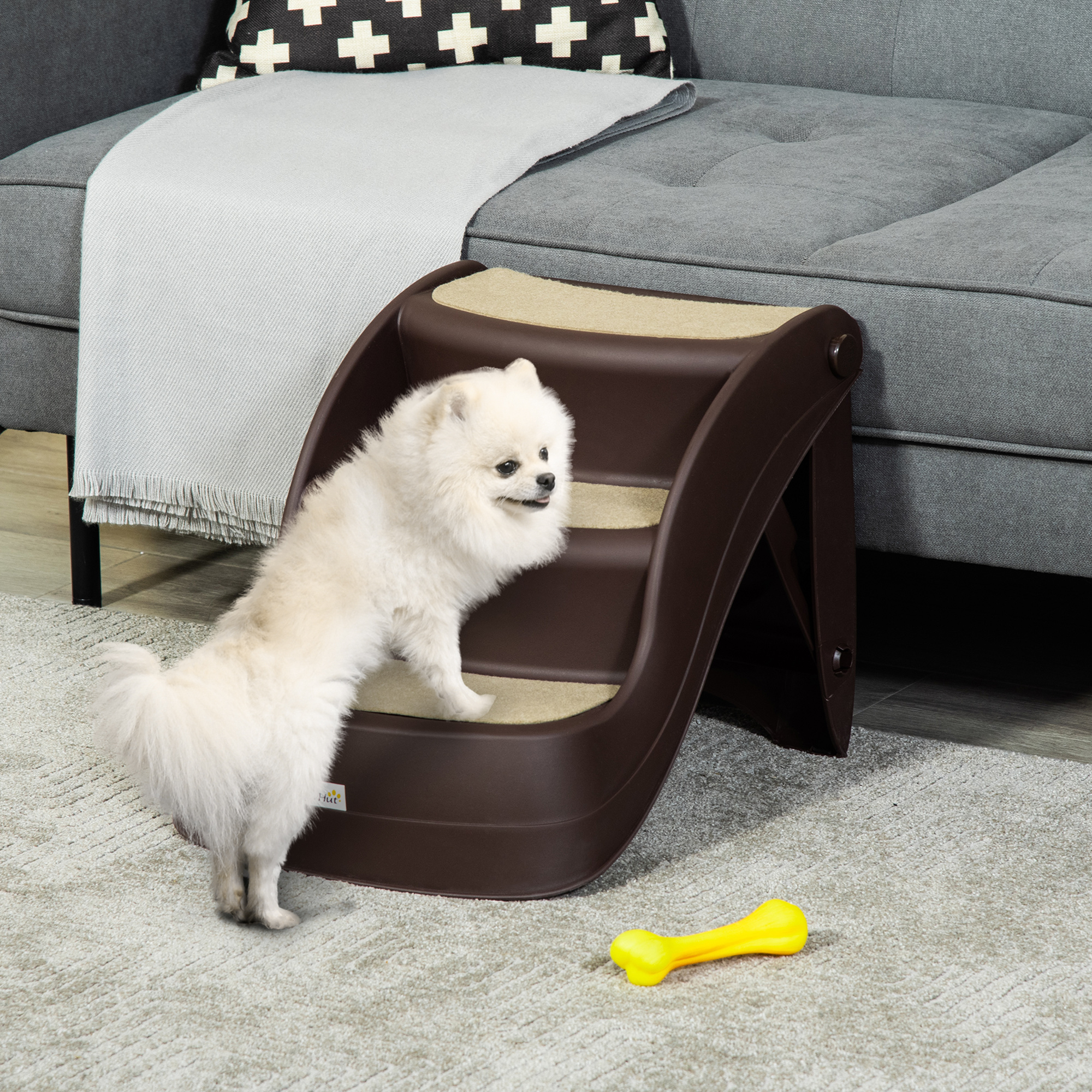 Un cachorro Pomerania blanco está en una escalera para perros marrón junto a un sofá.