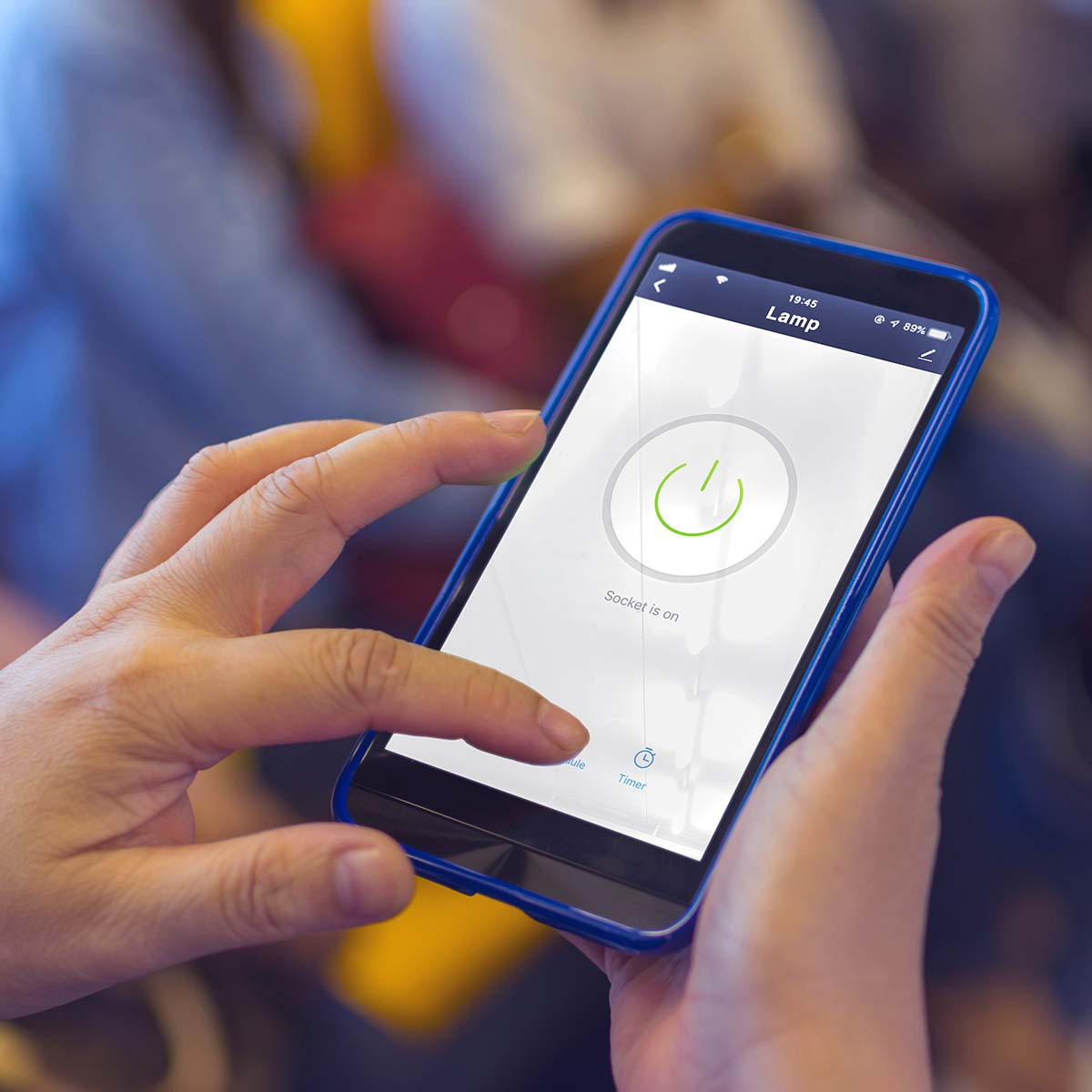 A hand holds a blue smartphone displaying a smart home app with a green power icon.