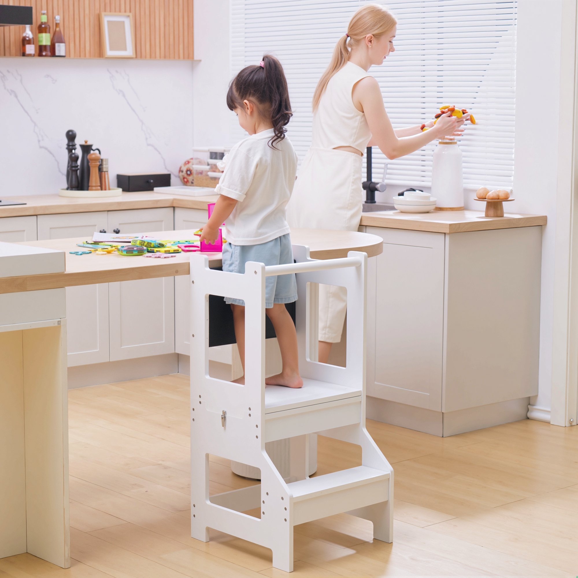 Niño en taburete escalón en cocina, madre limpia ventana. Juguetes en mesa.