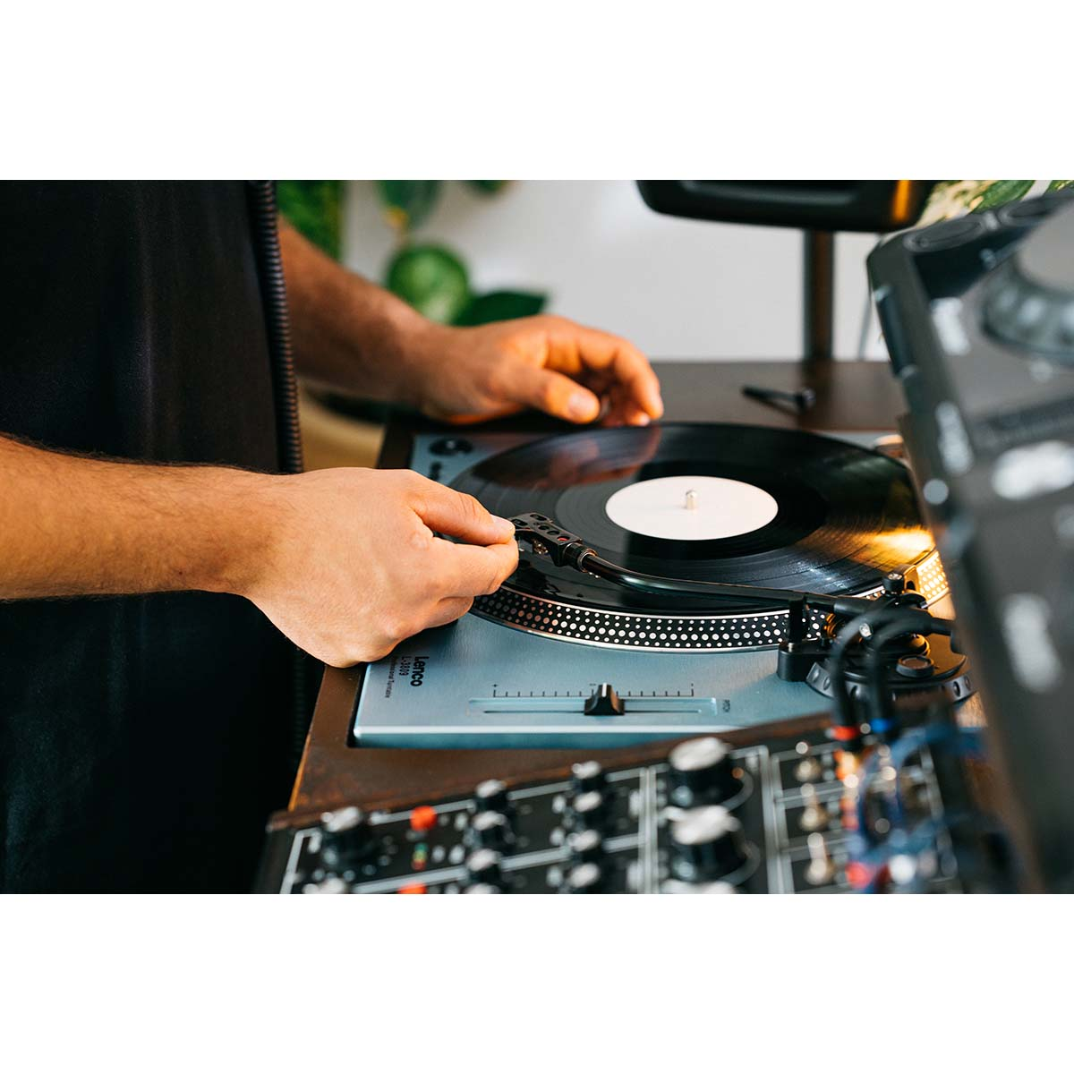 Mężczyzna kładzie płytę winylową na gramofonie, obok miksera DJ-skiego.