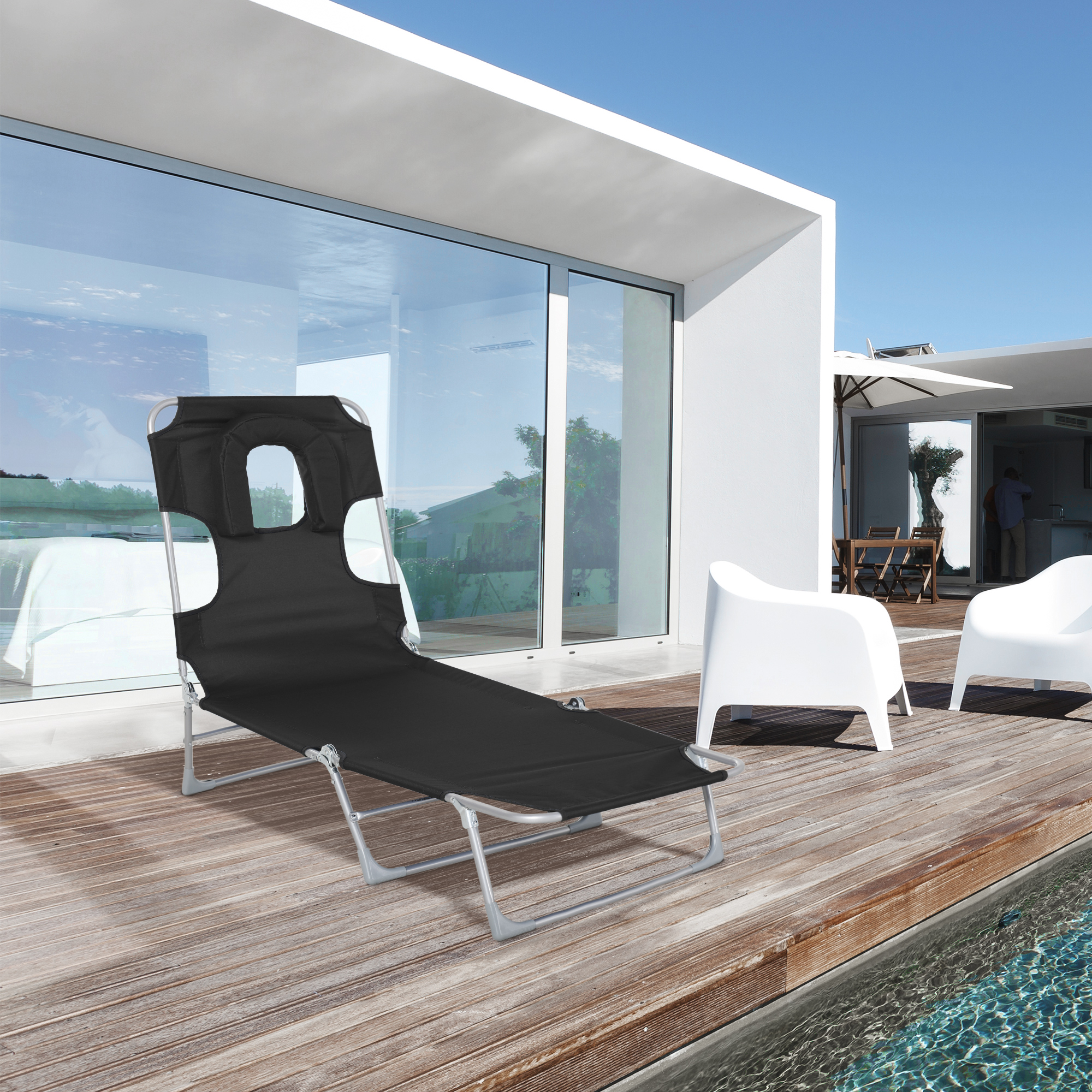 Tumbona negra sobre cubierta de madera con piscina y casa moderna.