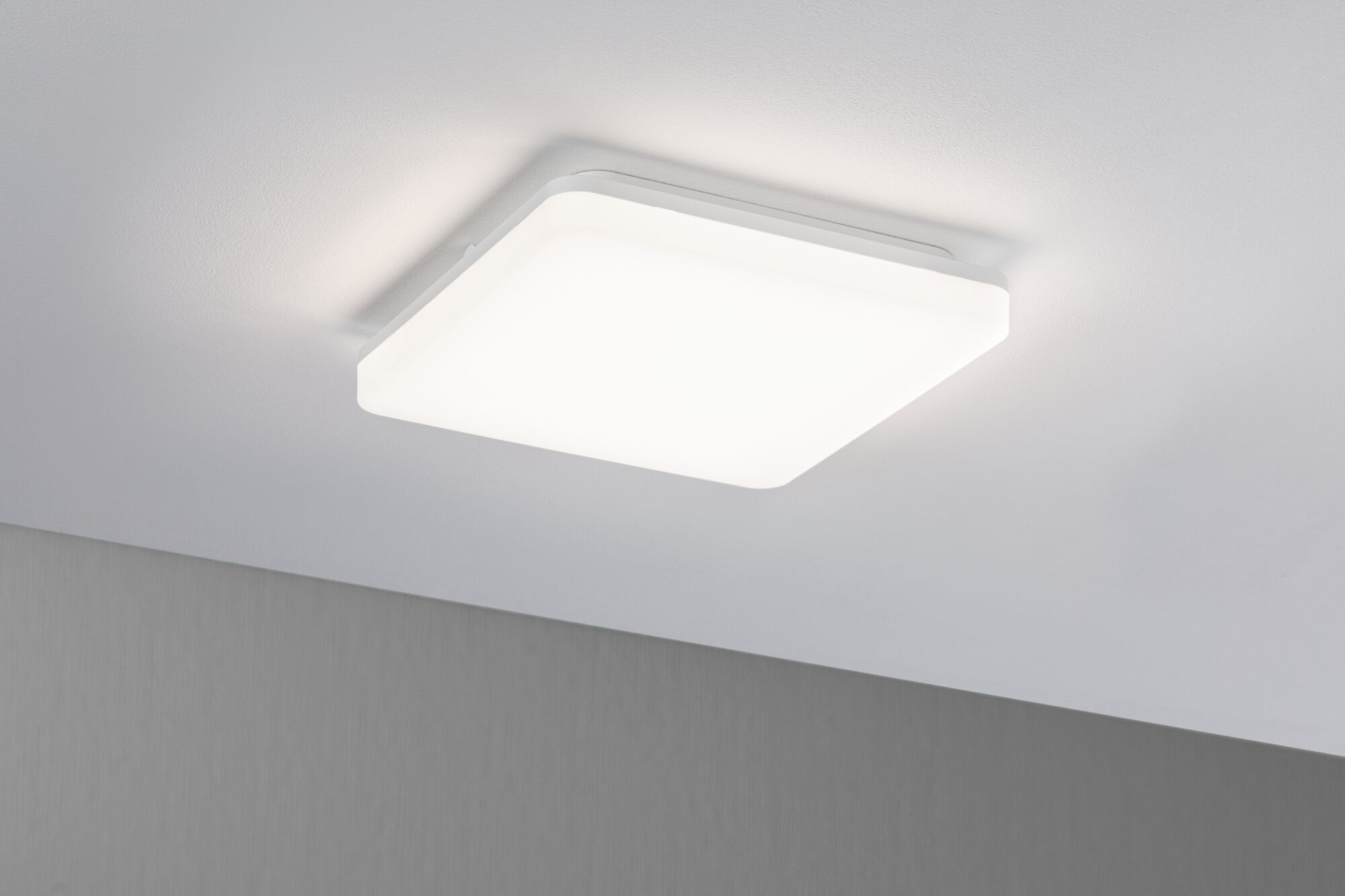 Eine weiße, quadratische Deckenleuchte mit diffusem Licht leuchtet auf einer weißen Decke.
