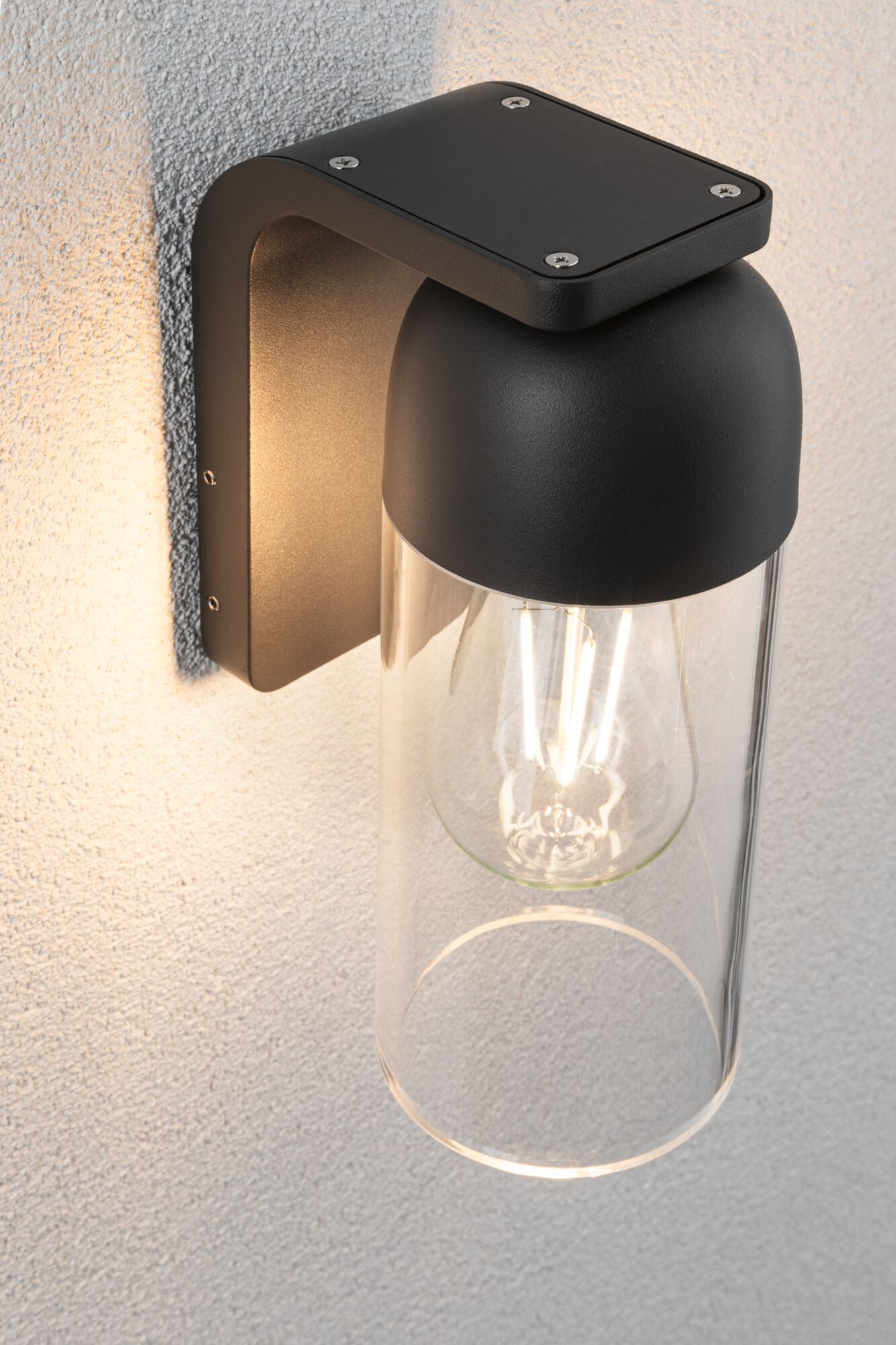 Czarna lampa ścienna z szklanym cylindrem i widoczną żarówką na teksturowanej ścianie.