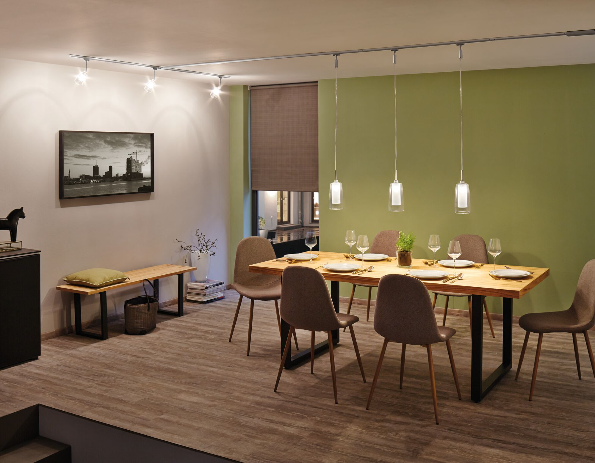 Sala da pranzo con tavolo in legno, sedie, illuminazione e opera d'arte.