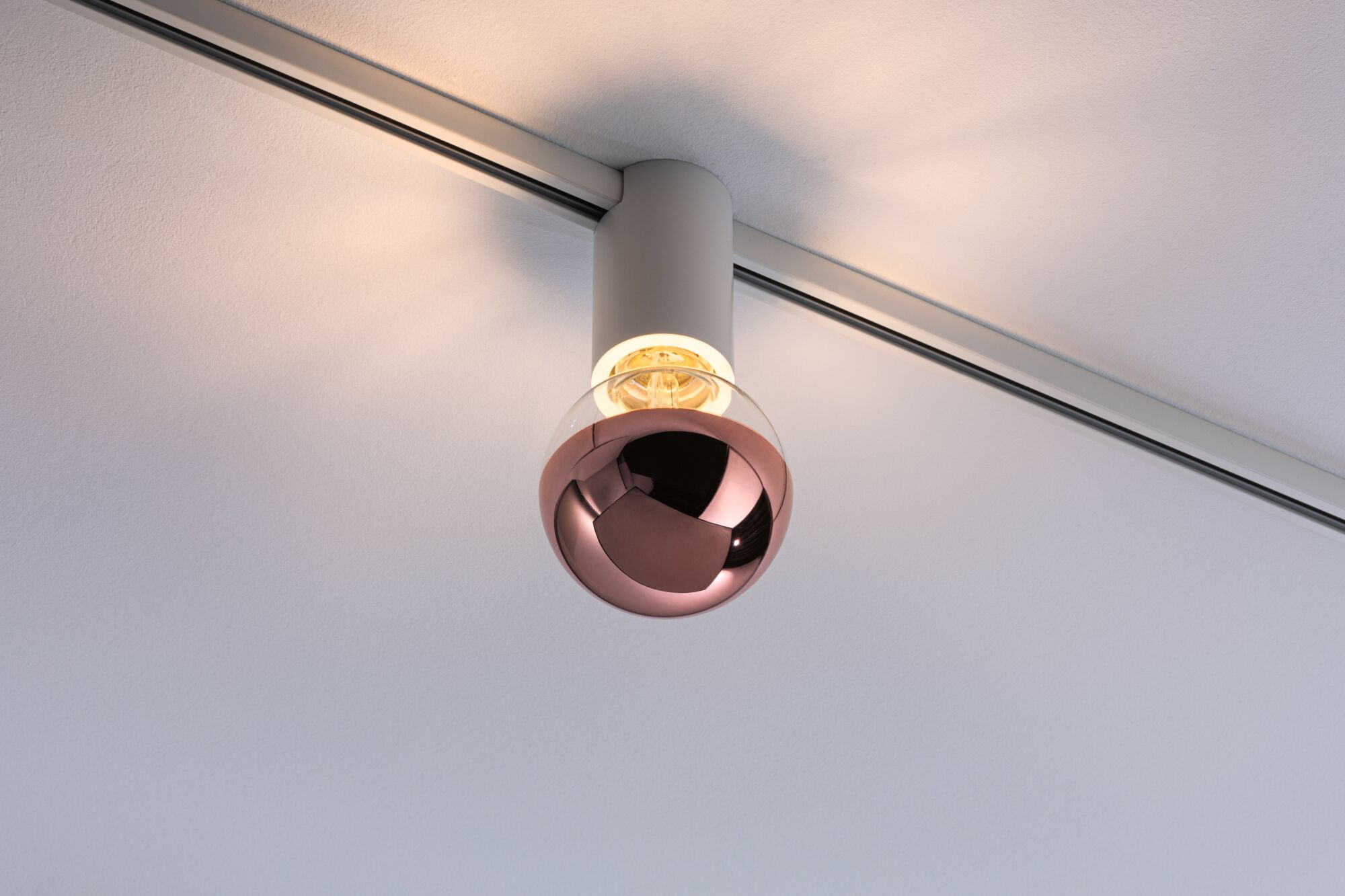 Eine kupferfarbene Kugel-Pendelleuchte an einer Schiene an der Decke.