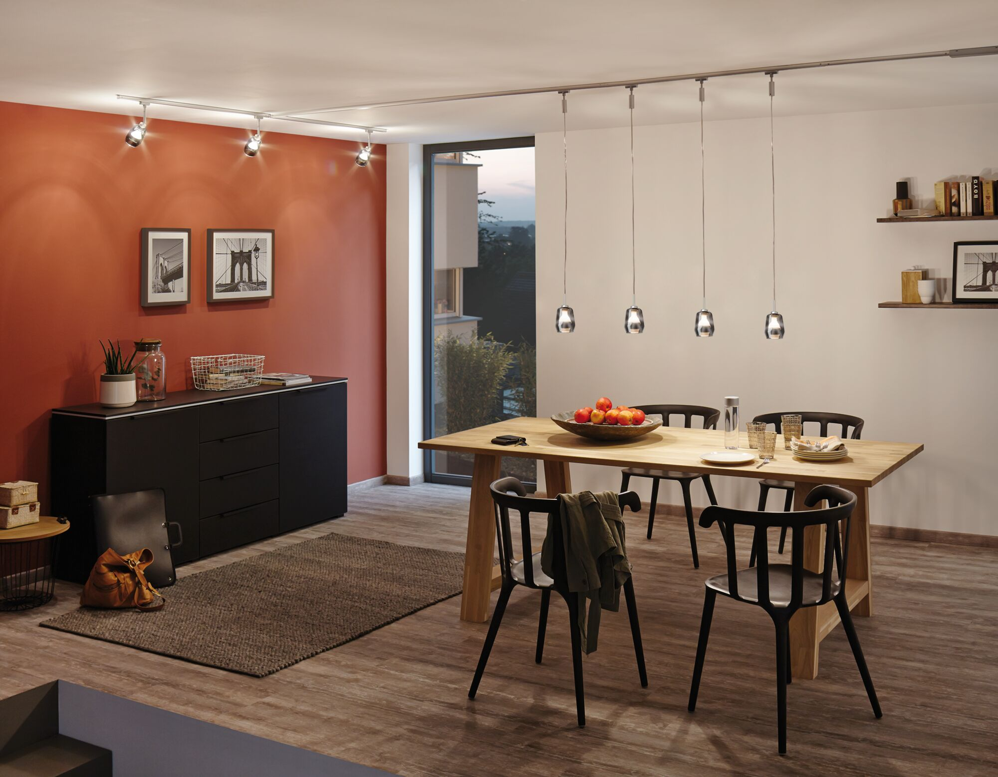 Ein Esszimmer mit Holztisch, schwarzen Stühlen, roter Akzentwand und Fenstern.