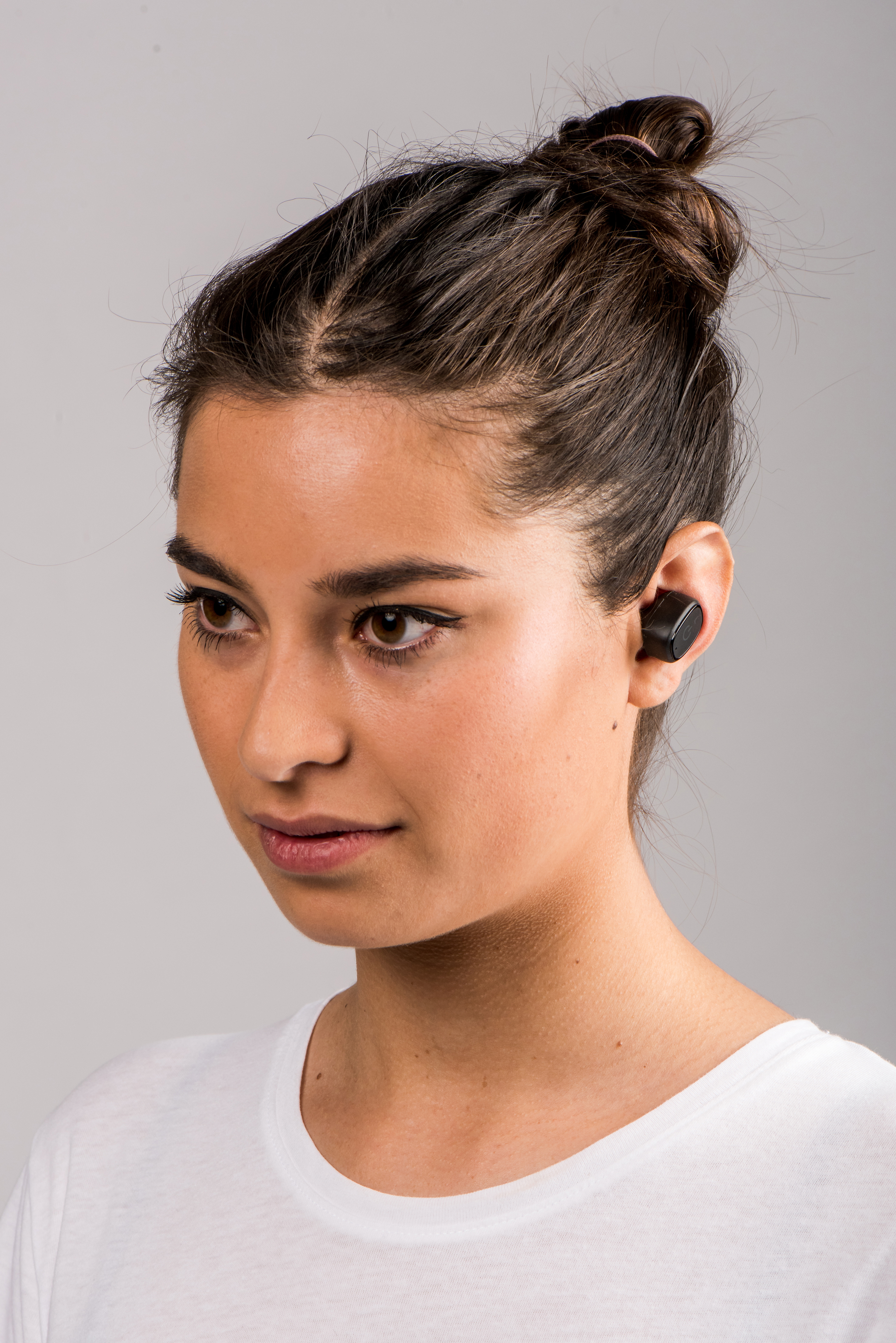 Junge Frau mit Dutt trägt weiße T-Shirt, schwarzes Earbud.