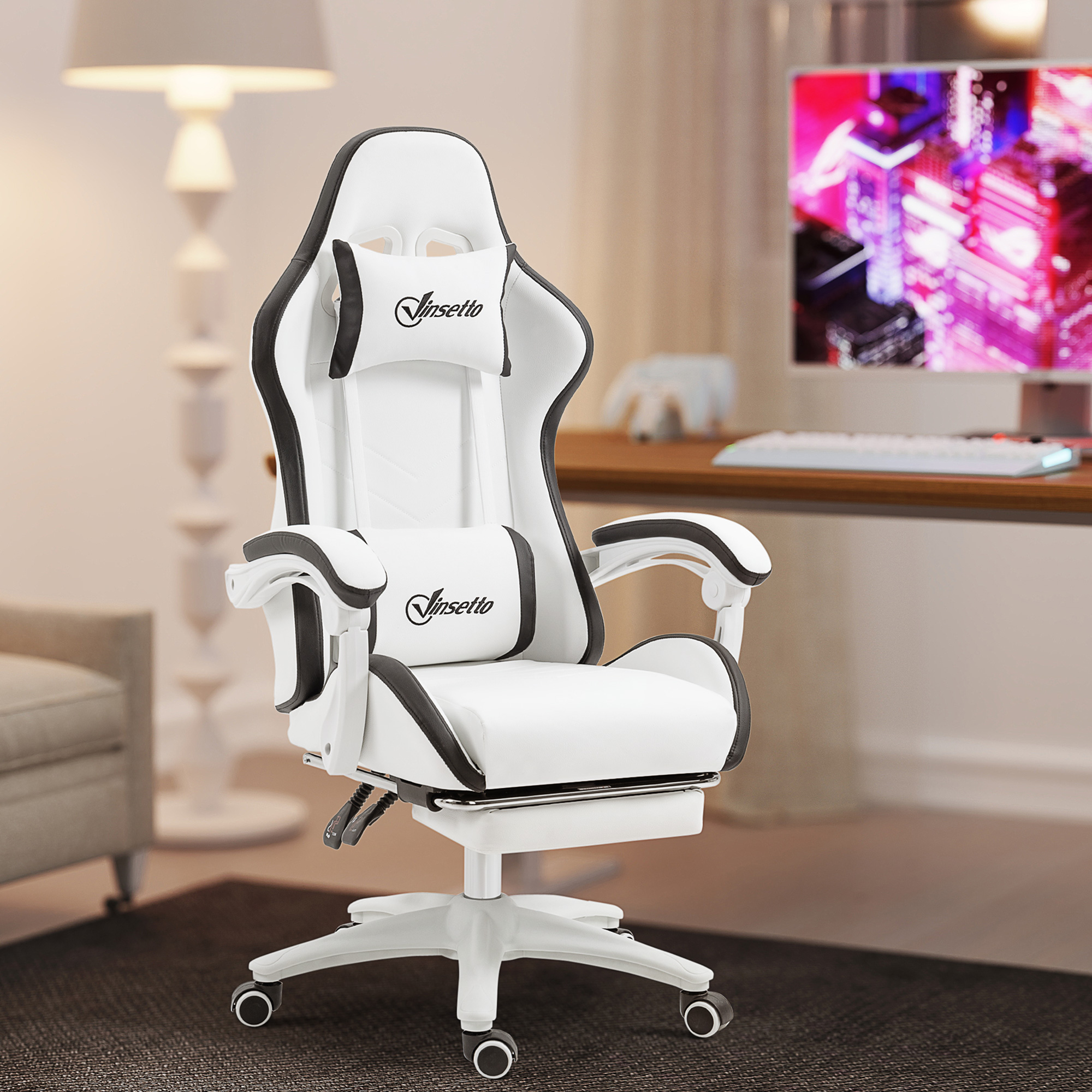 Una silla gamer blanca y negra con reposapiés está en una habitación con escritorio y monitor.
