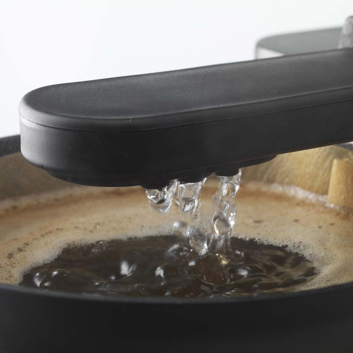 L'acqua gocciola da una macchina da caffè nera in un filtro con fondi di caffè marroni.